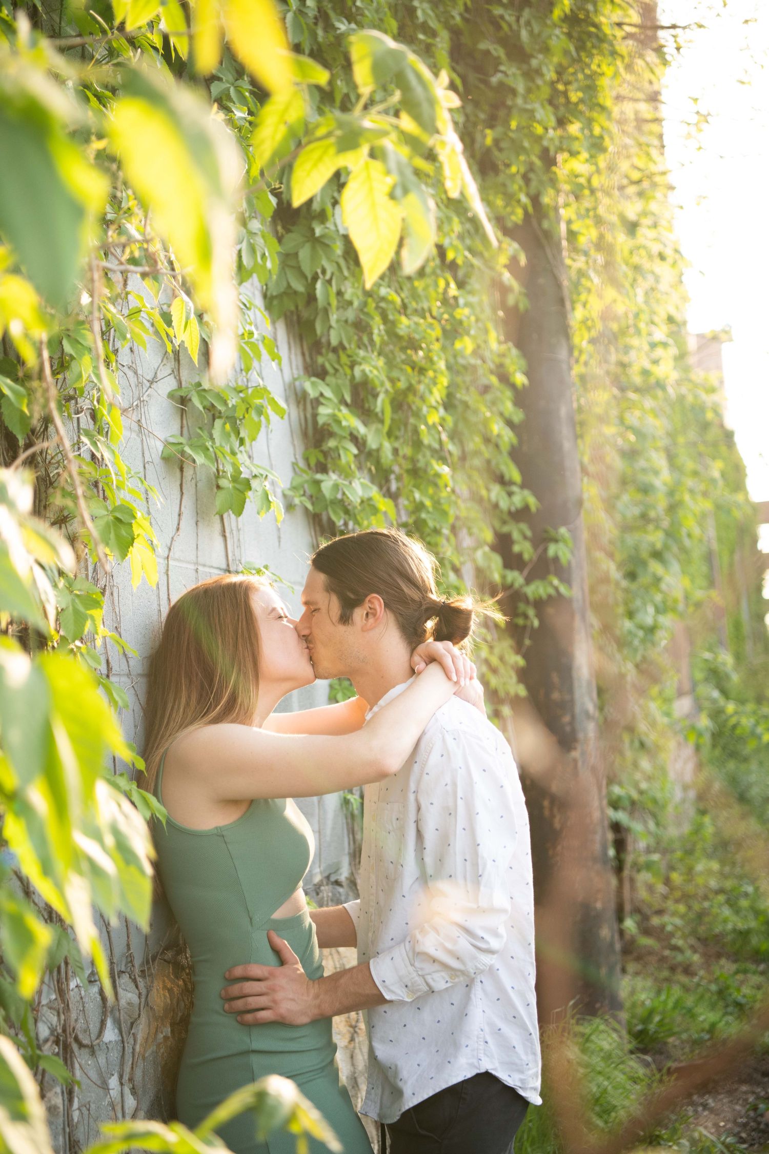 Intimate moment captured between couple surrounded by sunlit green leaves.