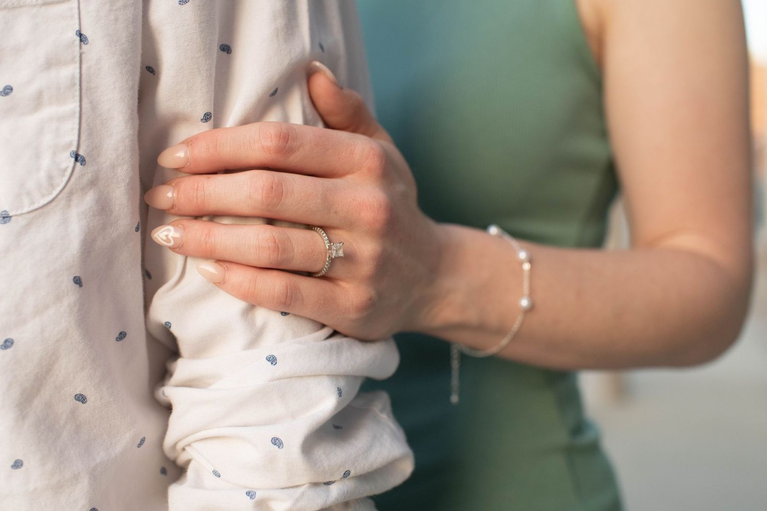 Close-up of hands with engagement ring against white shirt and mint green dress.