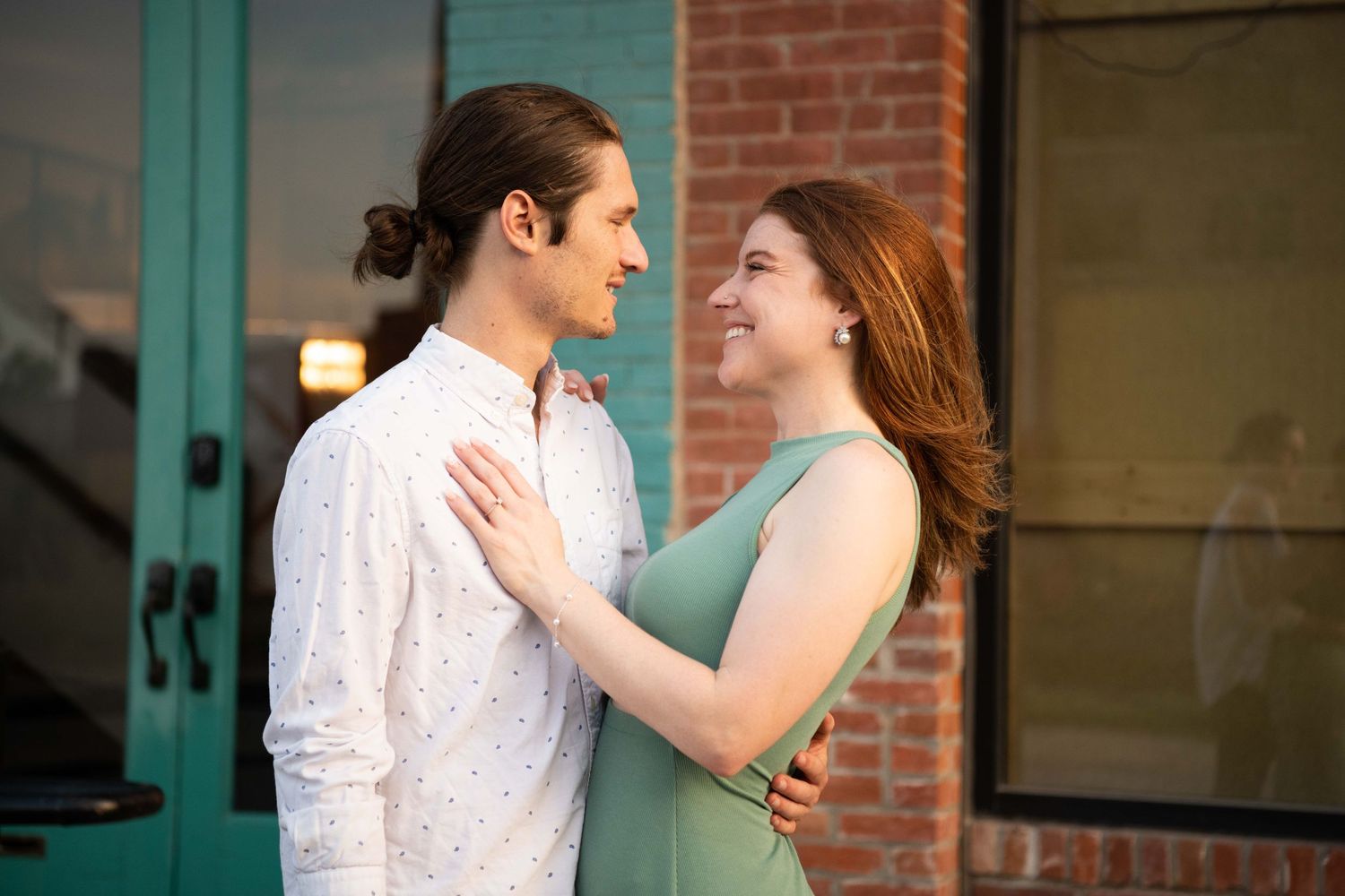 A couple shares a tender moment outside a brick building with turquoise accents.