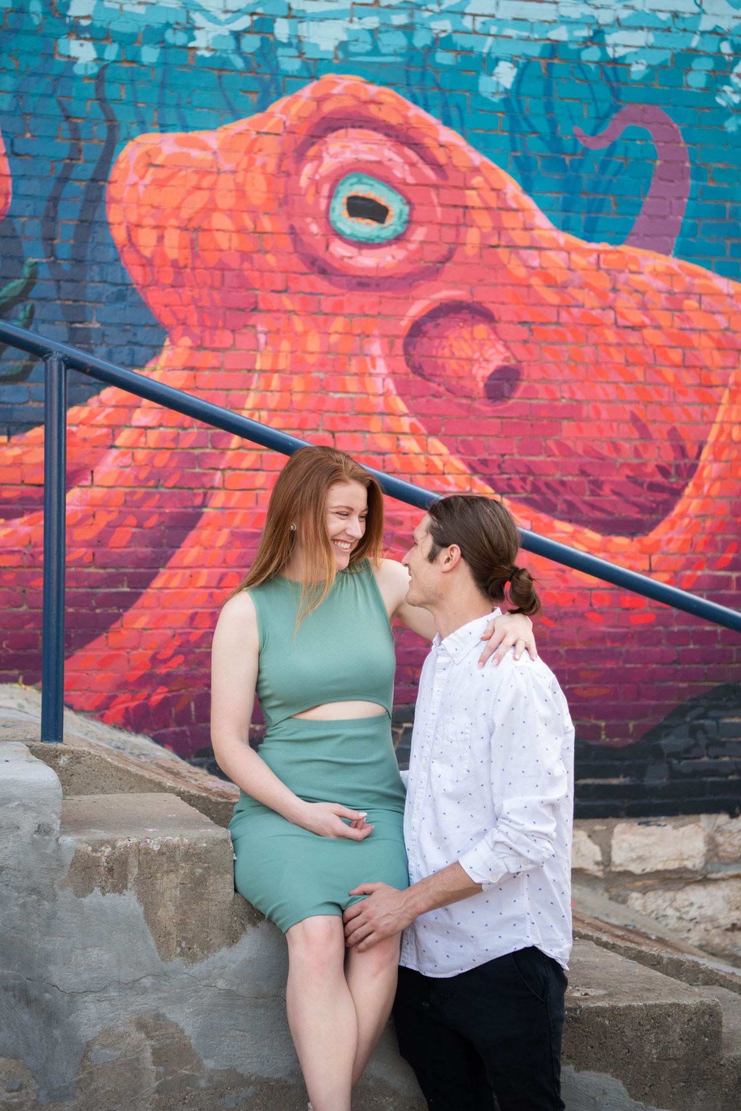 Couple poses in front of vibrant street art featuring large orange sea creature on blue background.