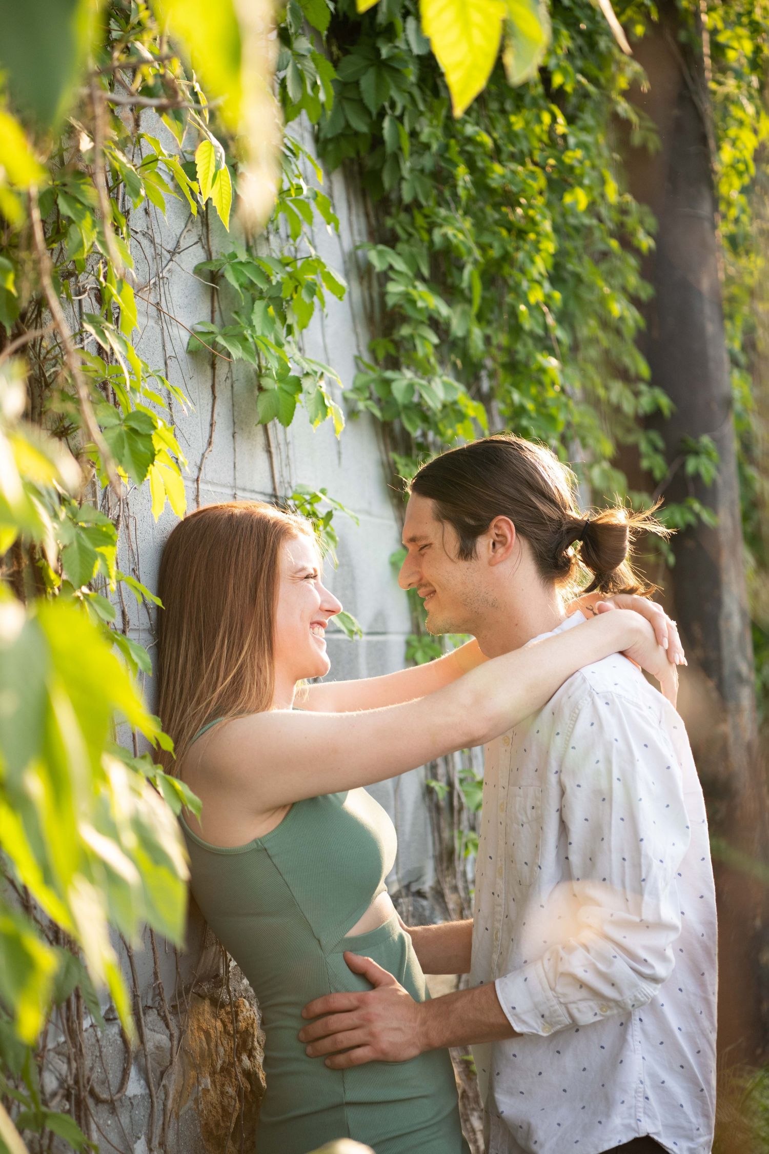 A joyful embrace between a couple framed by green leaves and sunlight.