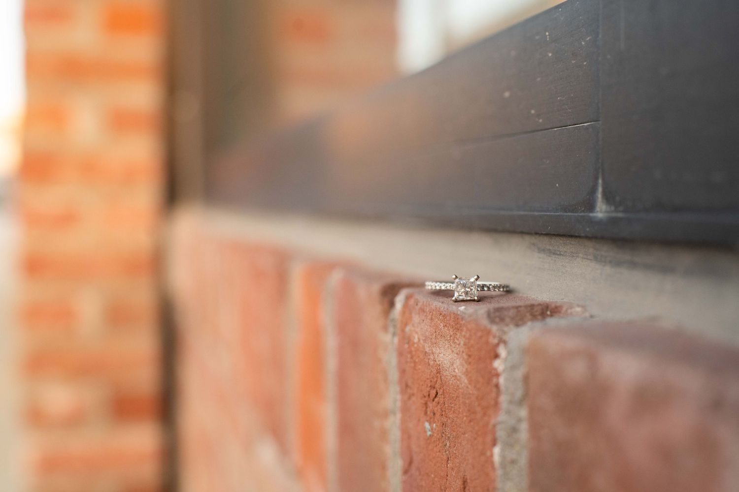 Close-up of an engagement ring sitting on a brick ledge with shallow depth of field.