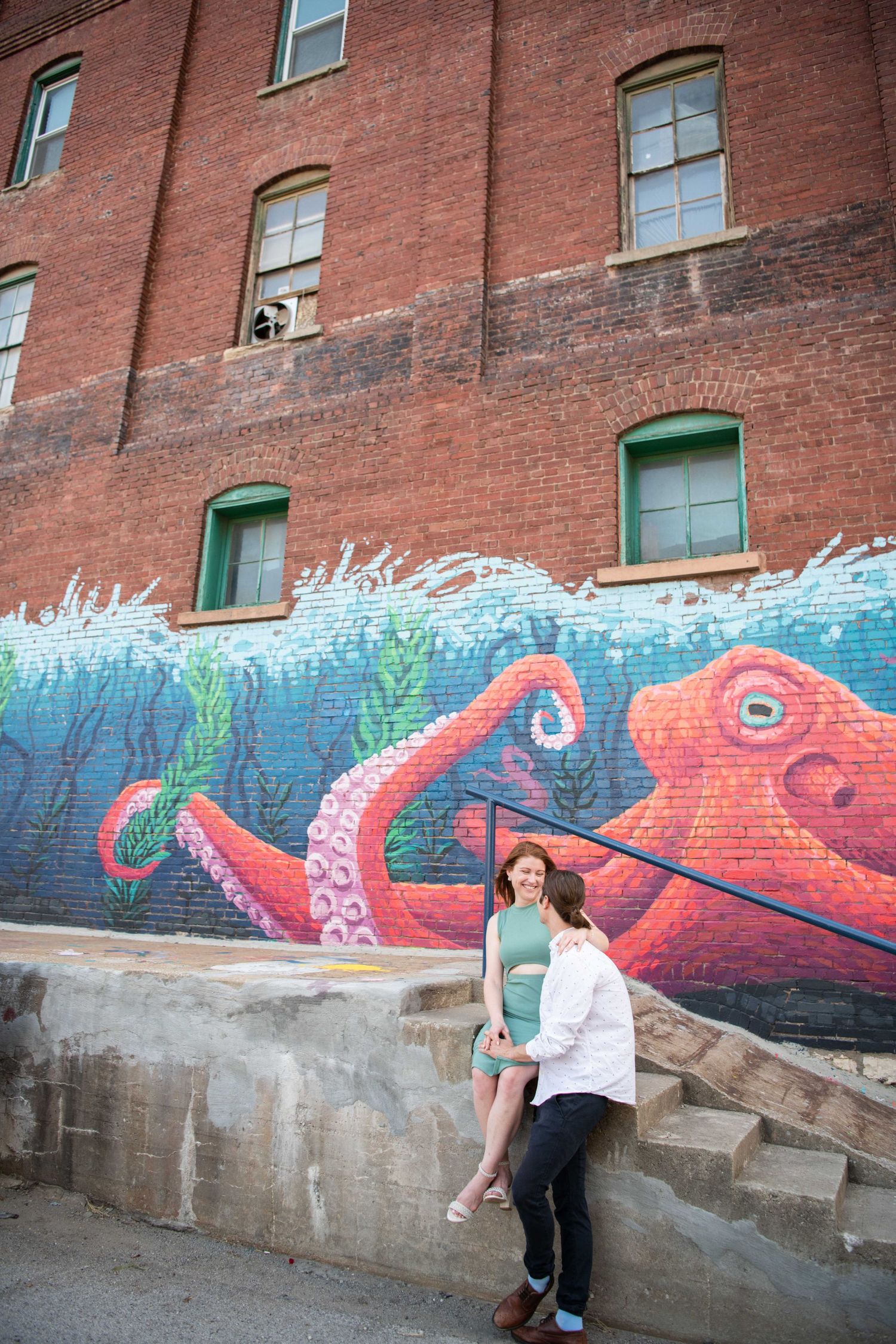 Couple poses against brick wall with vibrant ocean-themed street art featuring colorful octopi and sea waves.