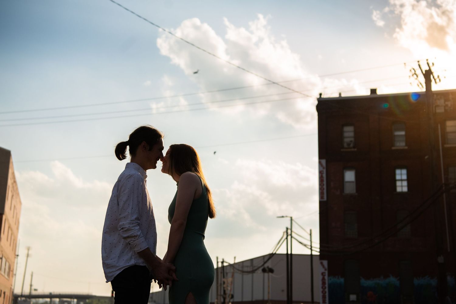 Couple in silhouette against dramatic sunset sky on urban railroad tracks.
