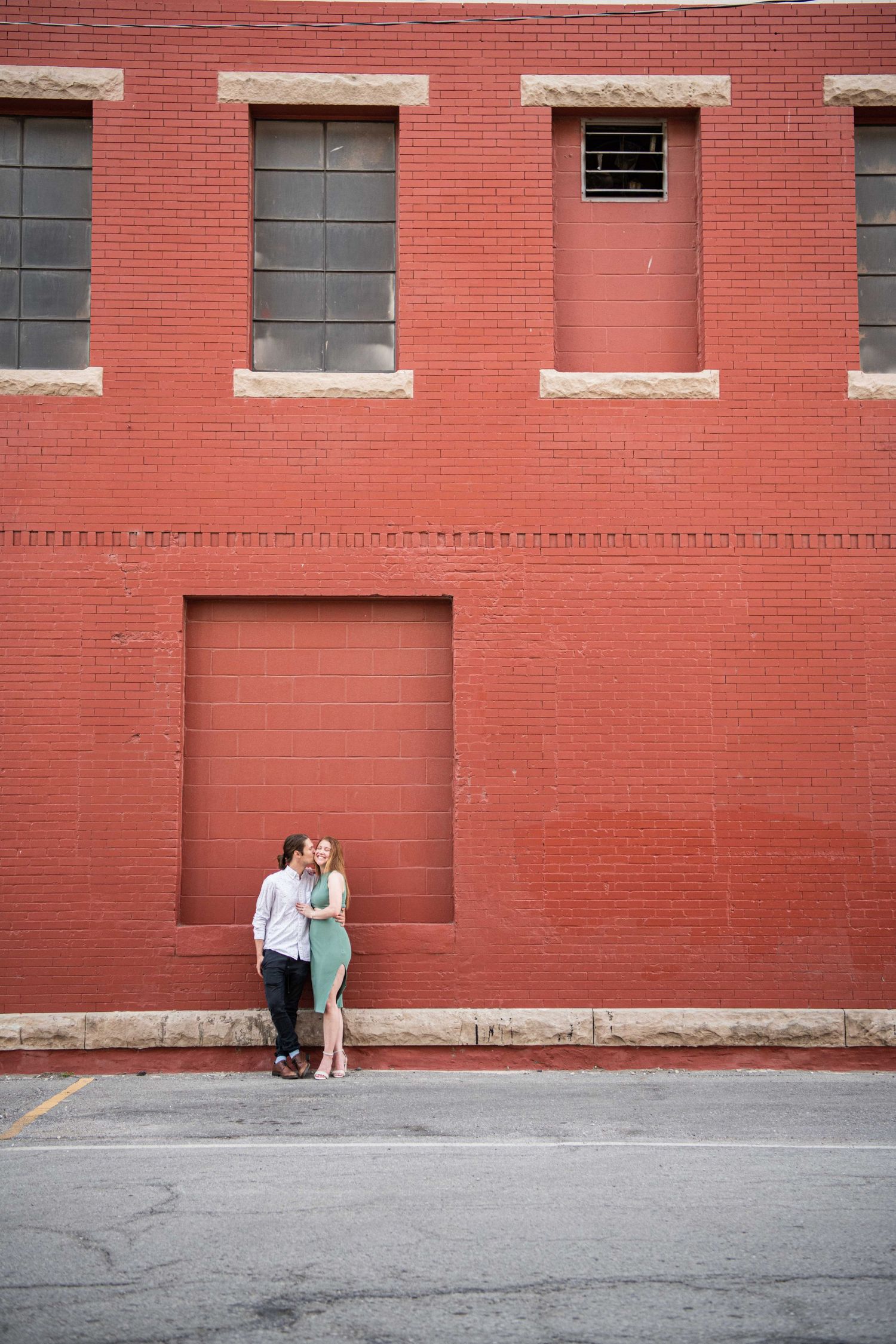 Couple stands in recessed doorway of industrial red brick building.
