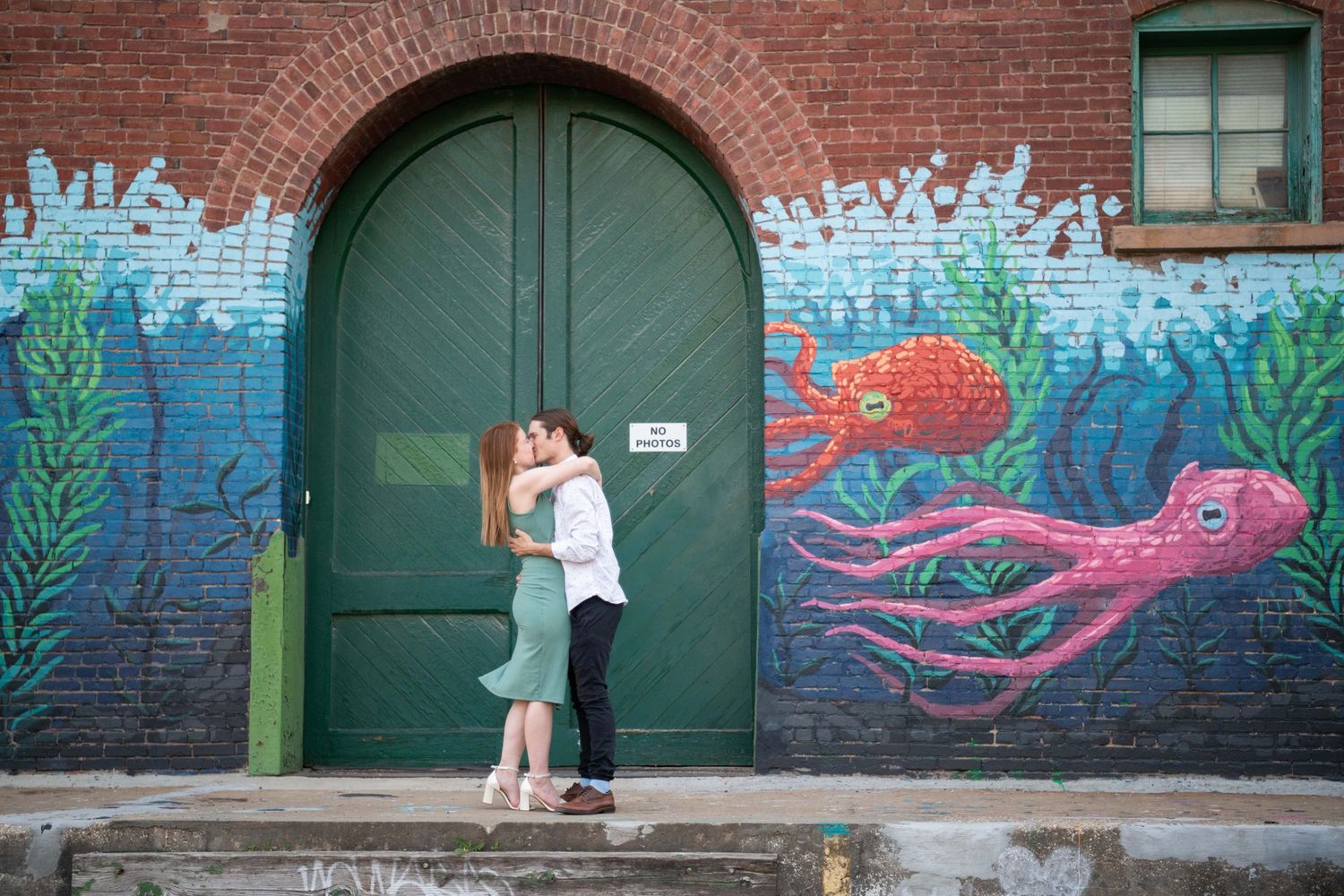 Romantic moment in front of green door with underwater mural featuring pink octopus tentacles.