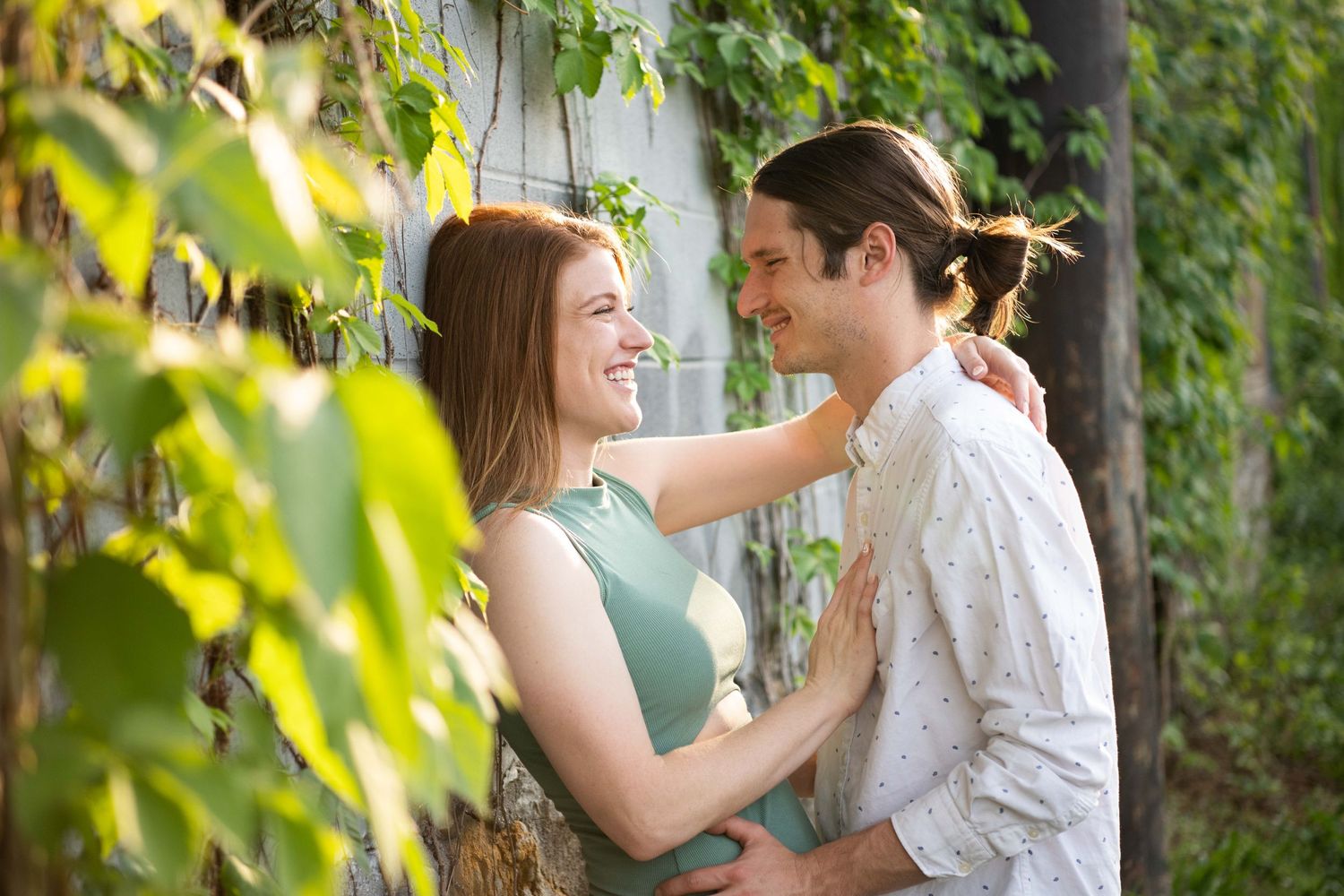 A romantic couple embraces among green ivy leaves on a sunny afternoon.
