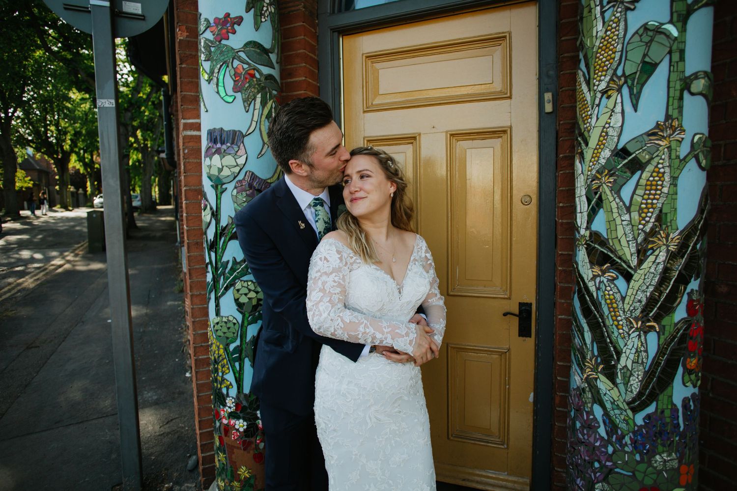 Wedding couple embracing by a yellow door surrounded by lush tropical plants.