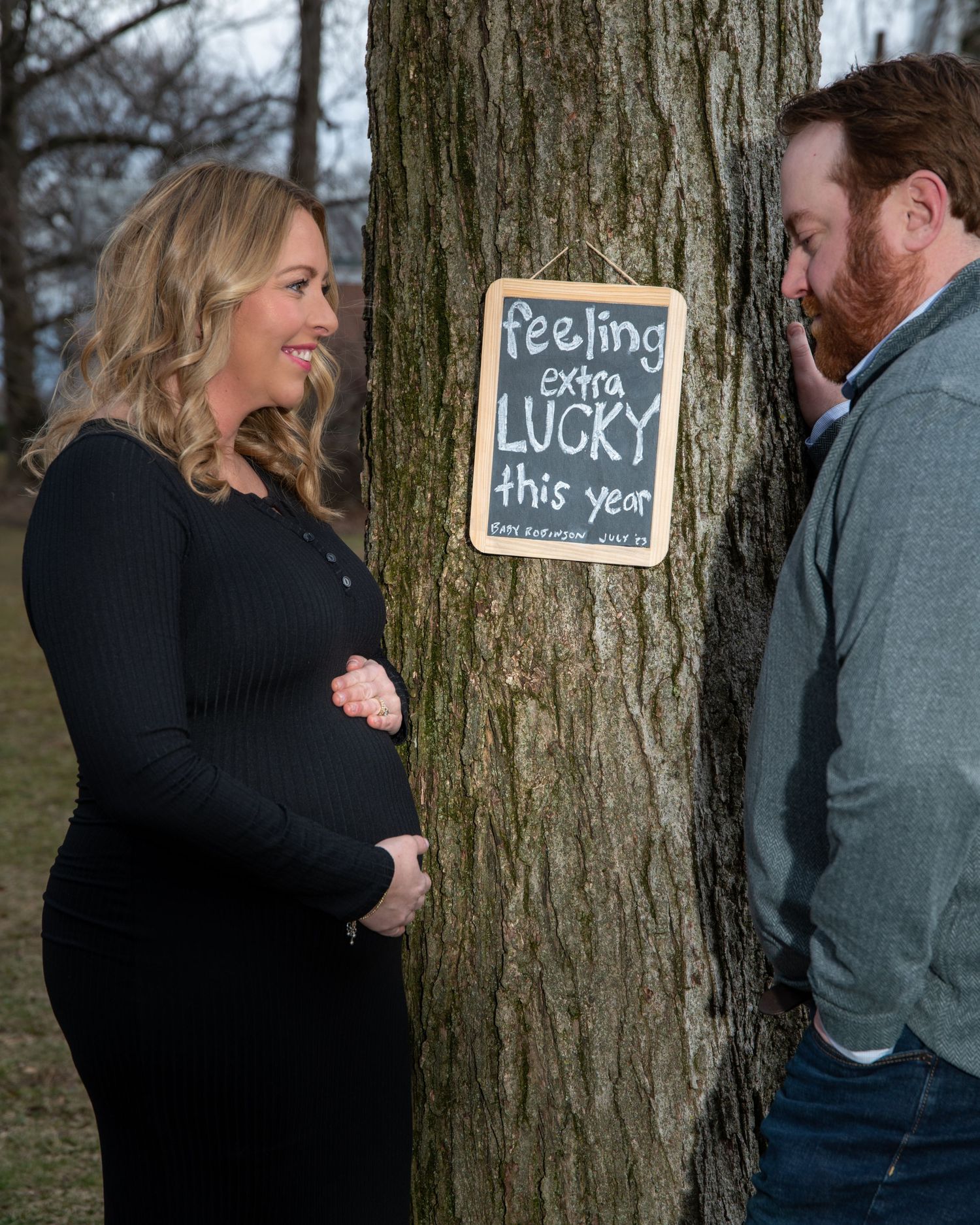 Couple poses by tree with chalkboard signs during outdoor photo session.