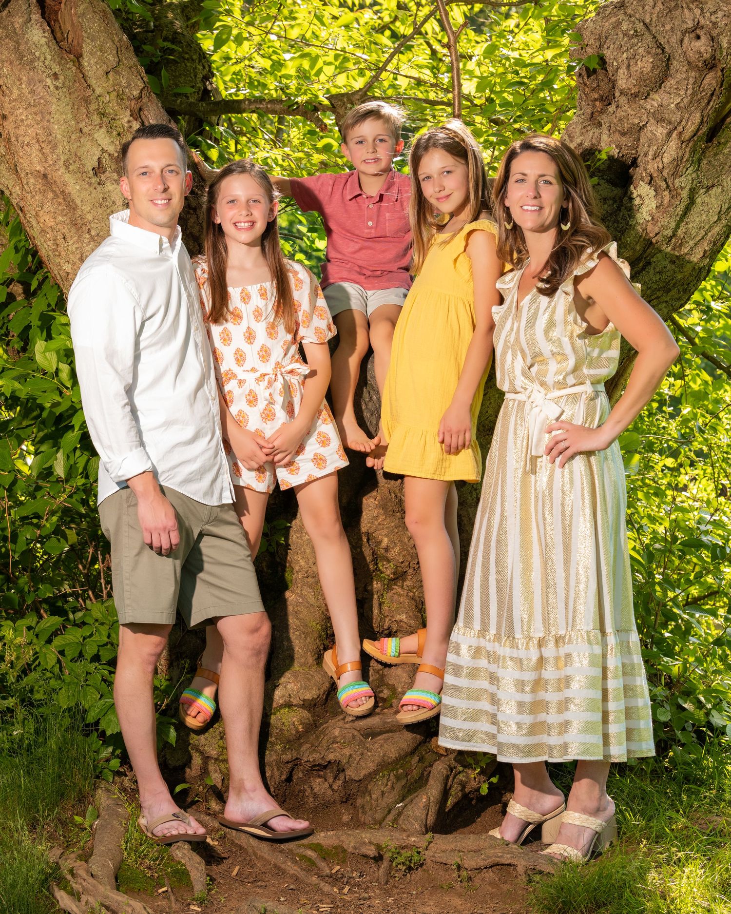 Family members' feet and legs shown while sitting on tree branch in summer setting.