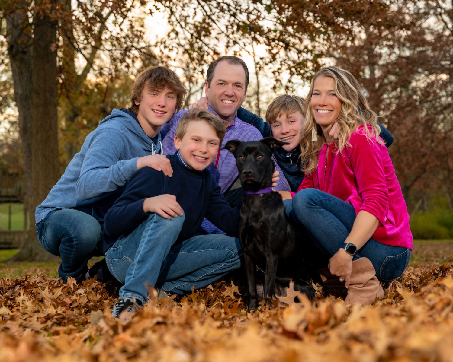 Family lying together on autumn leaves in a park during golden hour.