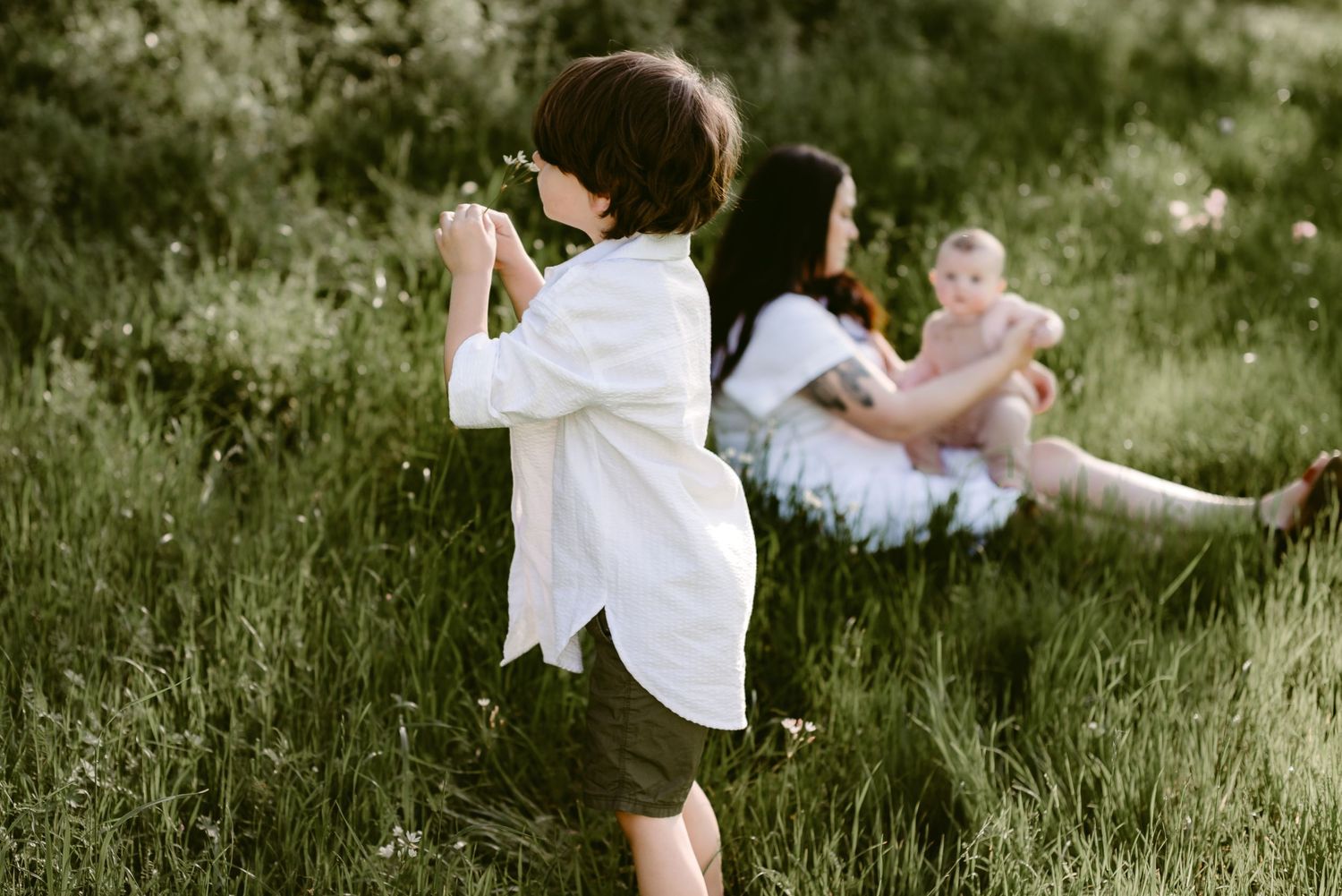 A Young Boy Smelling a Flower While A Mother and Baby Sit Behind Them in a Meadow in Seguin, Texas