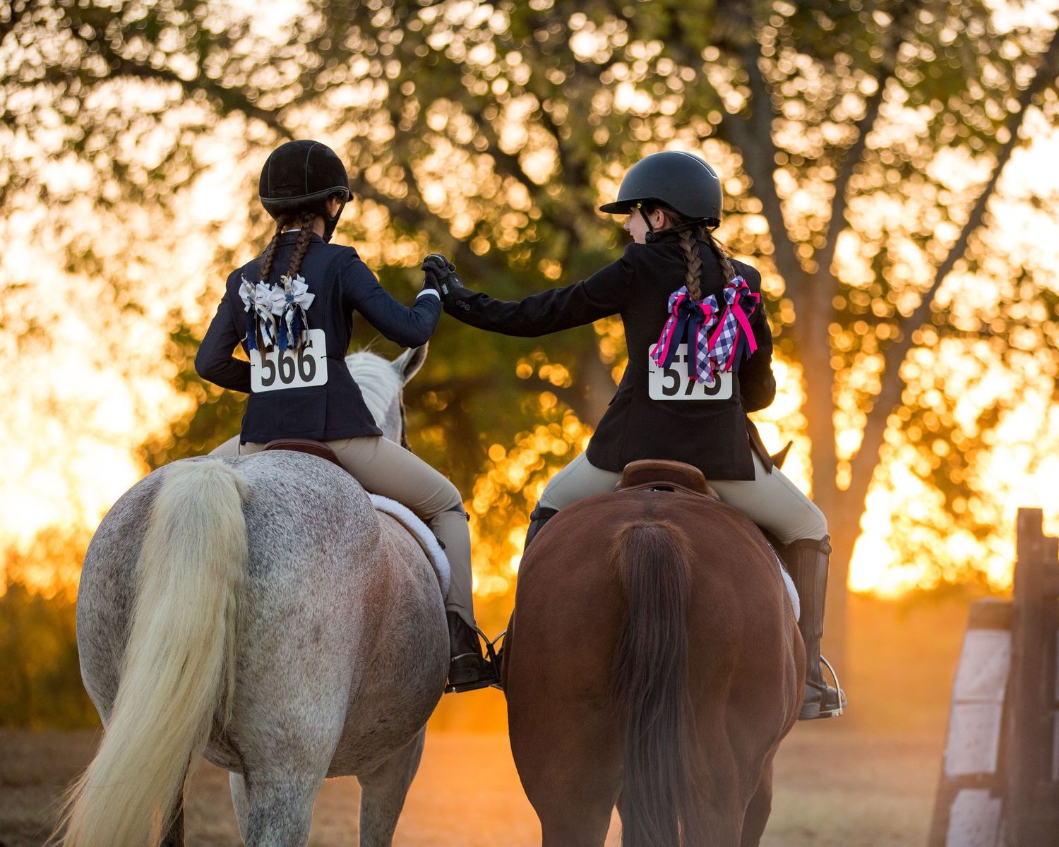 Two riders on horseback share a moment at sunset in outdoor arena.