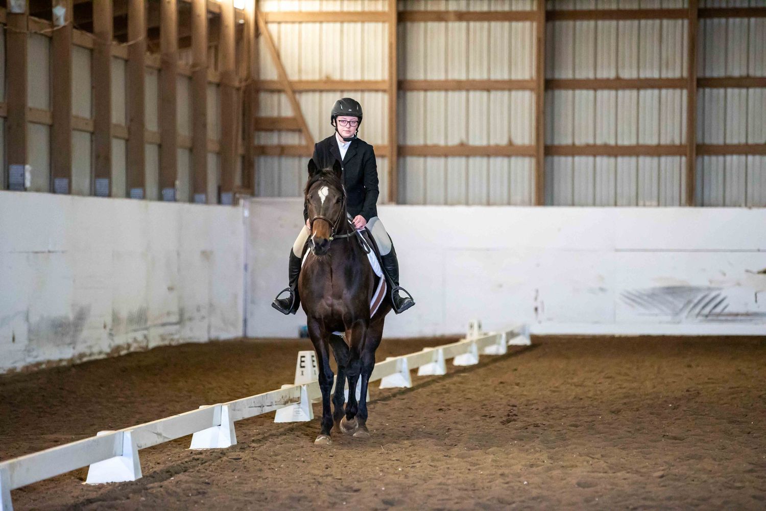 Dressage rider practicing with horse between white markers in indoor riding arena.