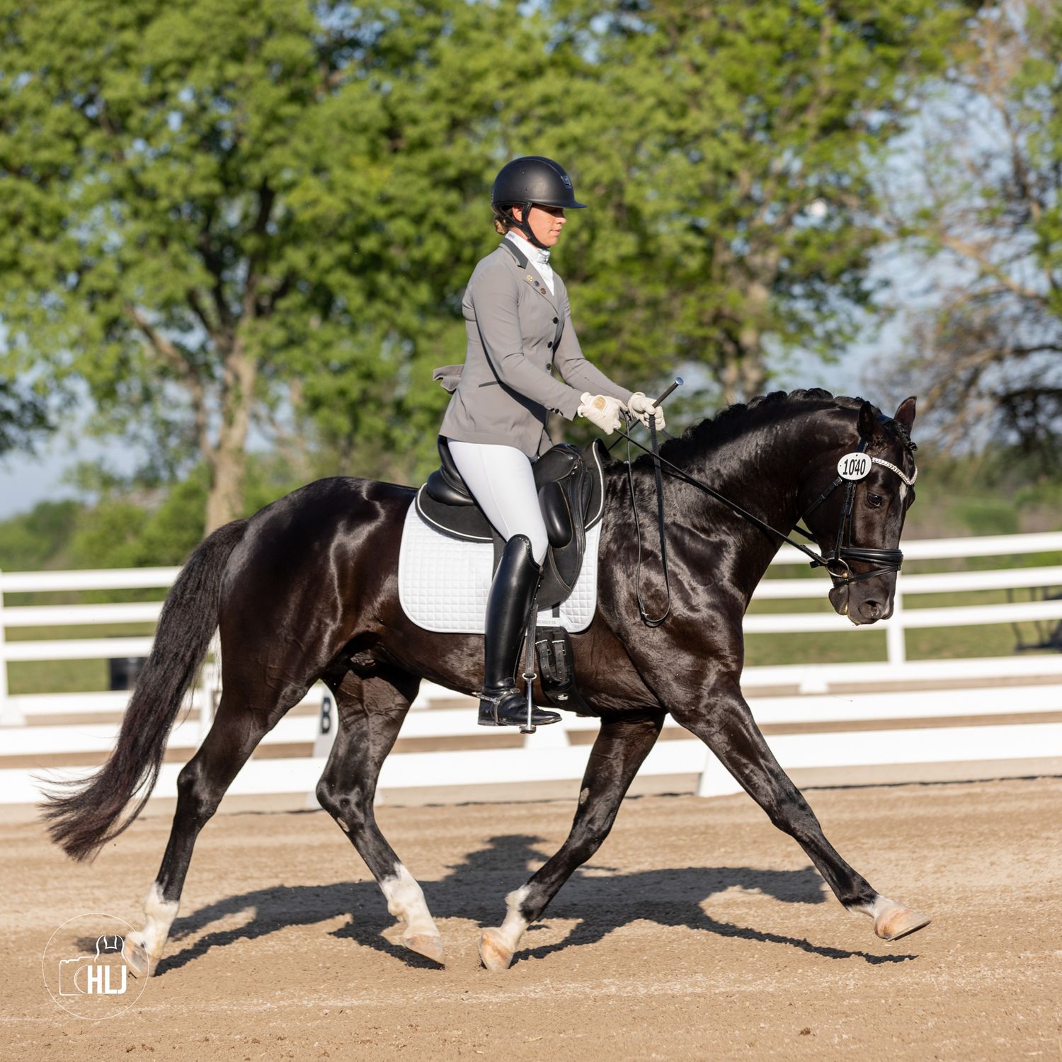 Rider in proper dressage attire performs a collected trot on elegant black horse in outdoor arena.