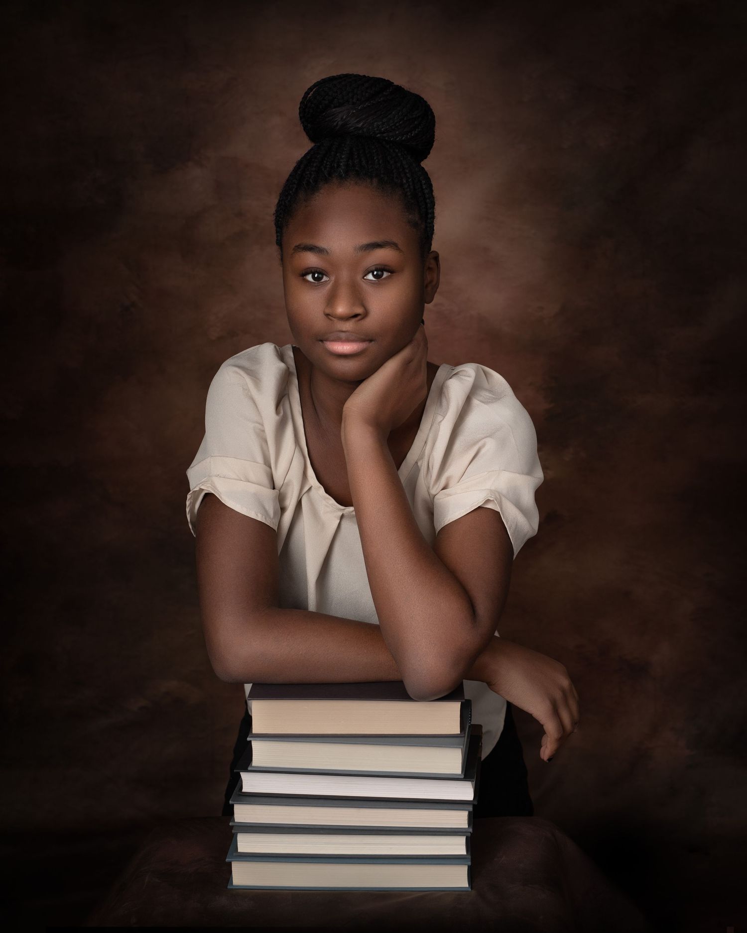 Artistic portrait of young person resting chin on stack of books against dark background.