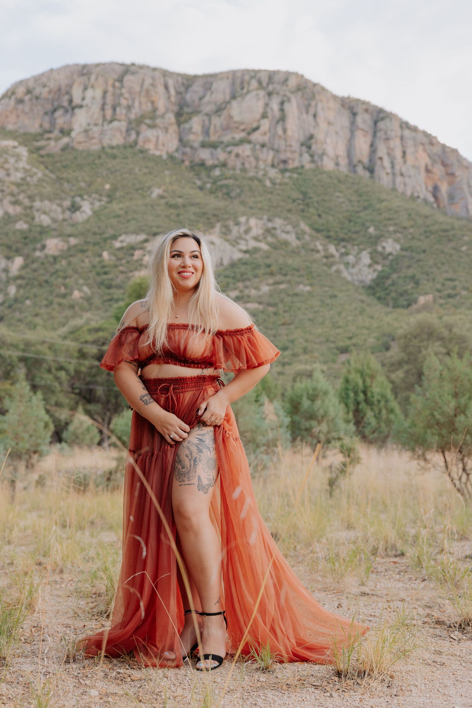 Orange sheer dress flows in desert setting with dramatic mountain cliffs.