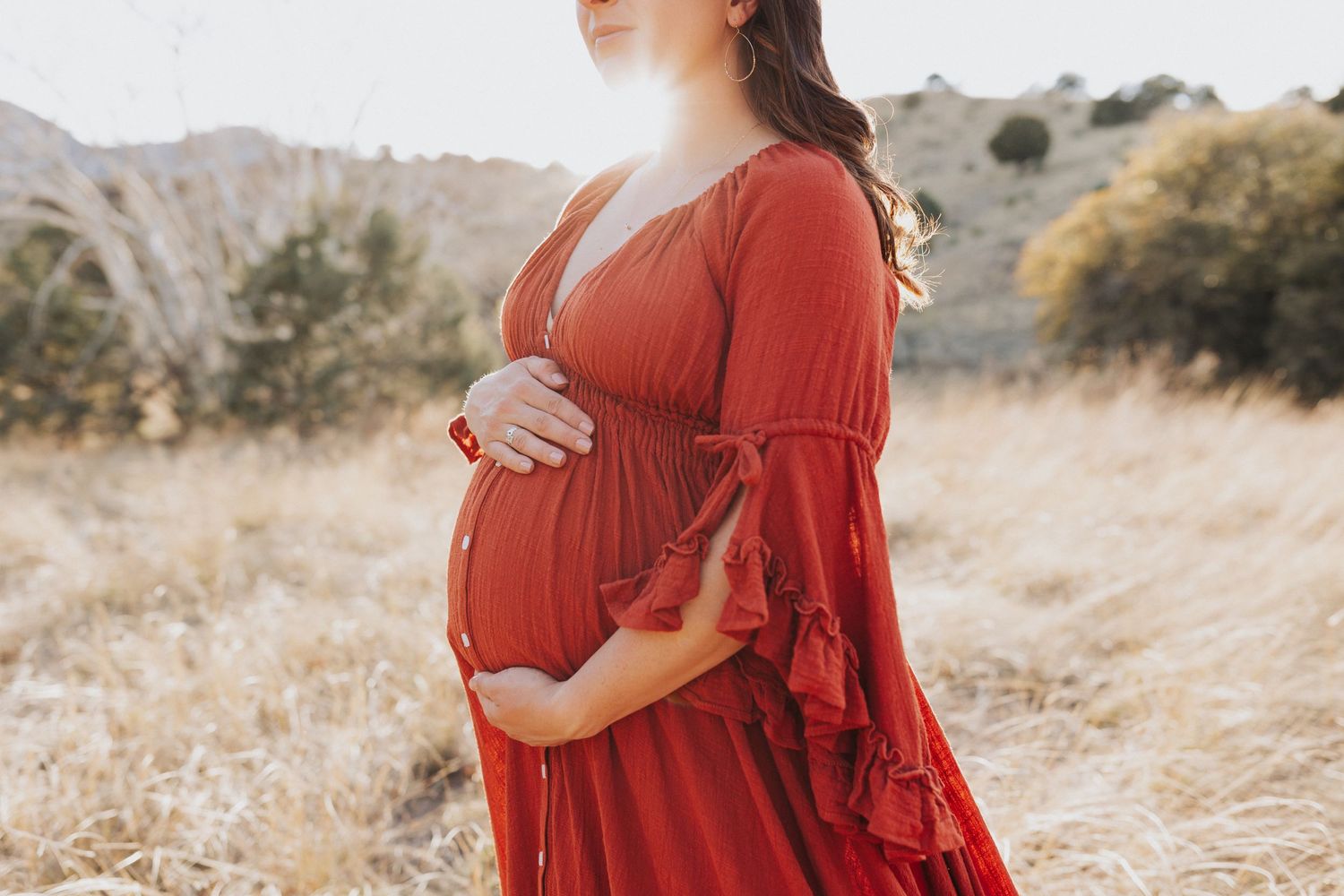 A maternity portrait featuring a red maxi dress in a sun-drenched desert setting.