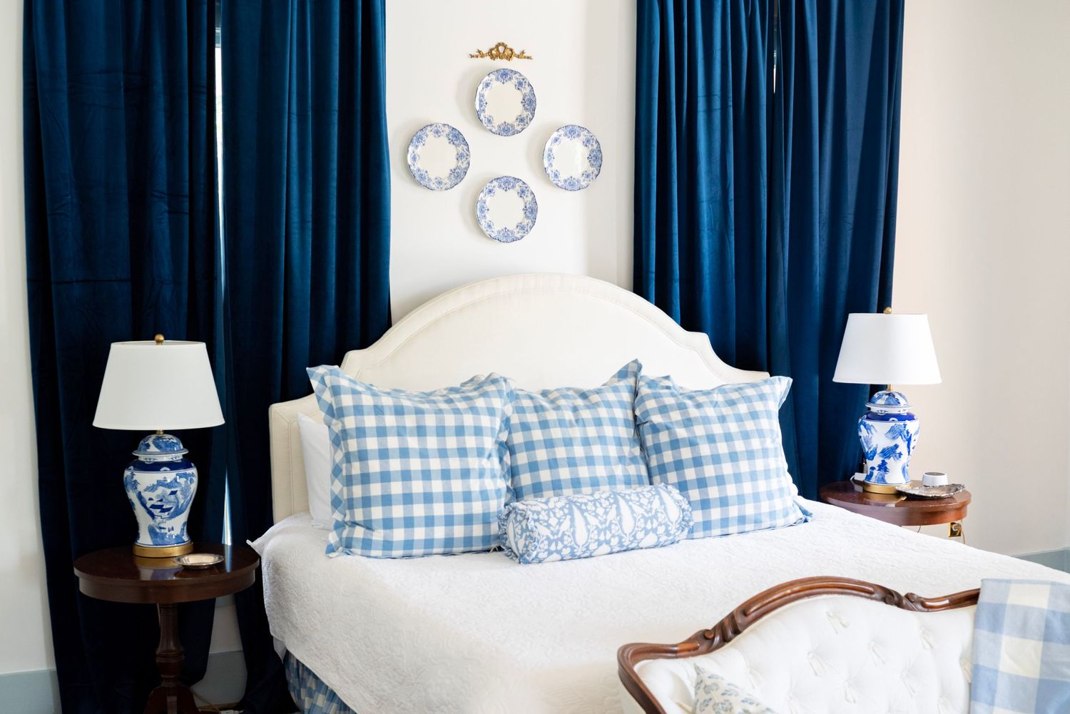 Bedroom with navy curtains, white headboard, and blue gingham pillows in coastal style.