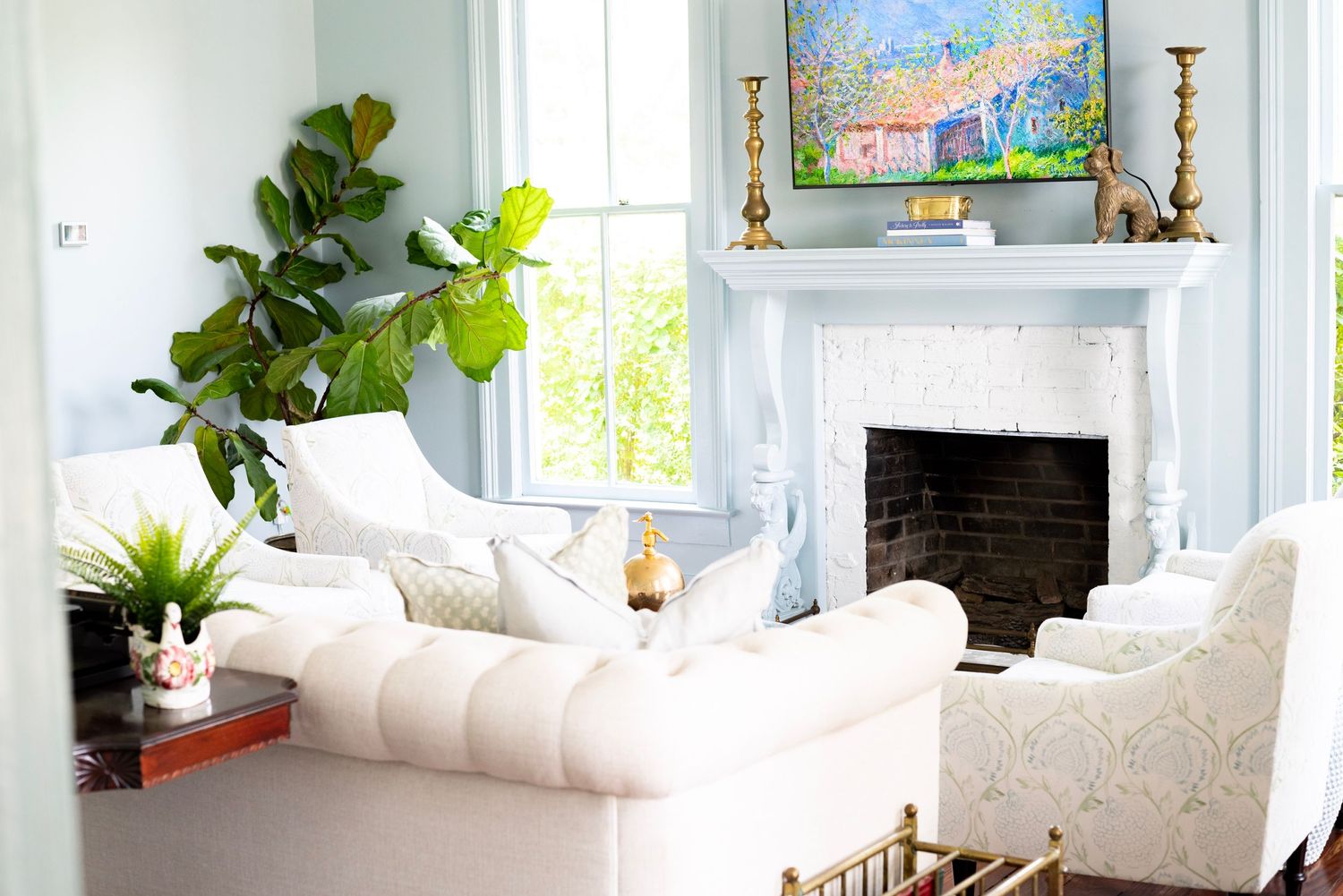 Bright living room with white furniture, fiddle leaf fig plant, and decorative fireplace mantel.