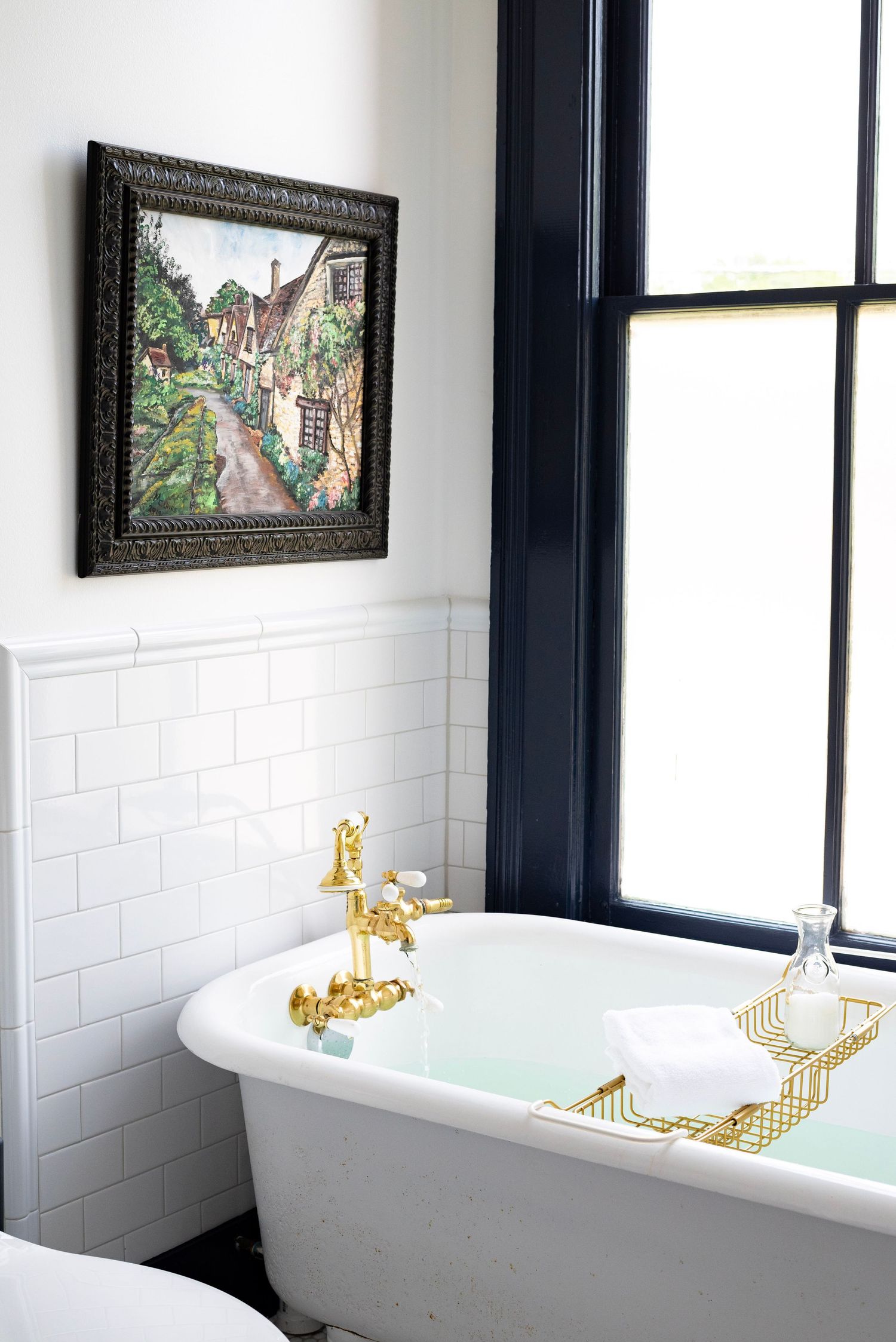 Classic clawfoot bathtub with gold fixtures beneath framed artwork in modern bathroom.