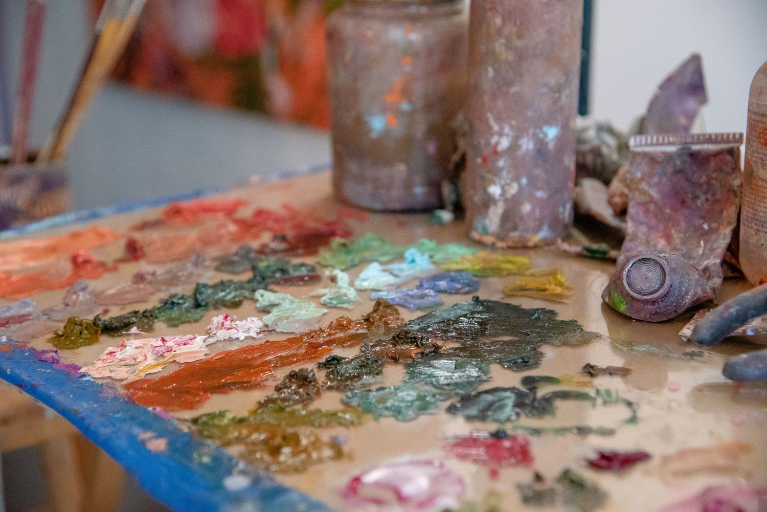 Paint-stained art studio workspace with various tools and materials scattered across the surface.