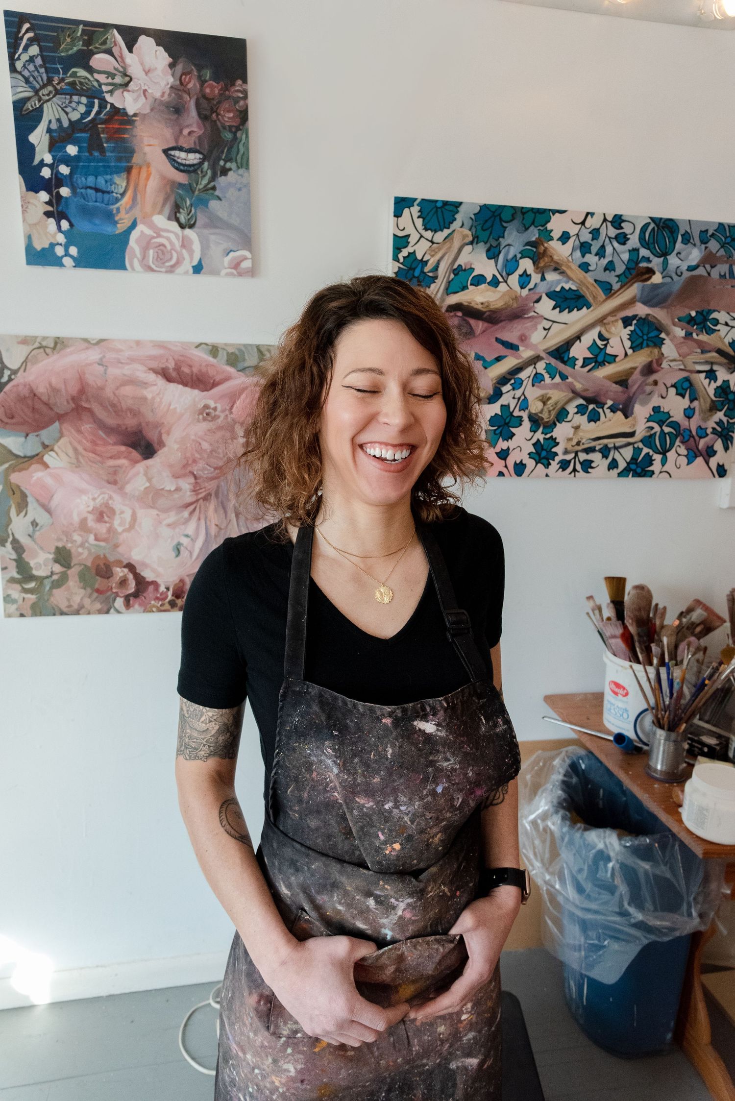 Artist wearing paint-splattered clothes works cheerfully in their creative studio space.