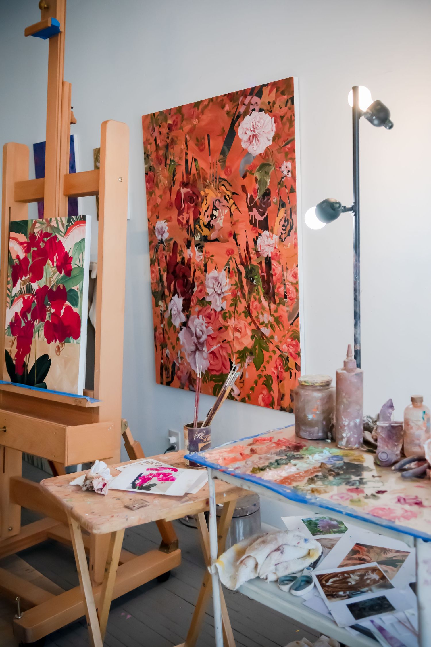 Art studio setup with wooden easels displaying vibrant orange and pink floral paintings.
