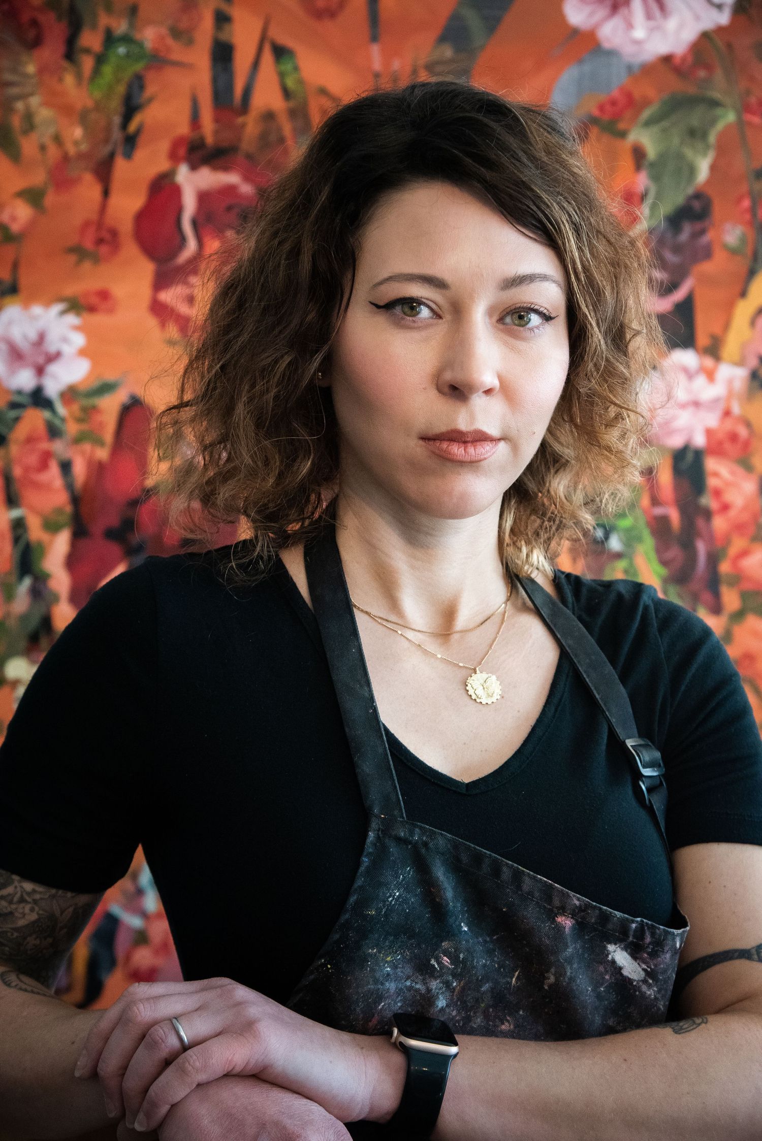 Artist in black shirt poses against vibrant orange floral backdrop in portrait series.