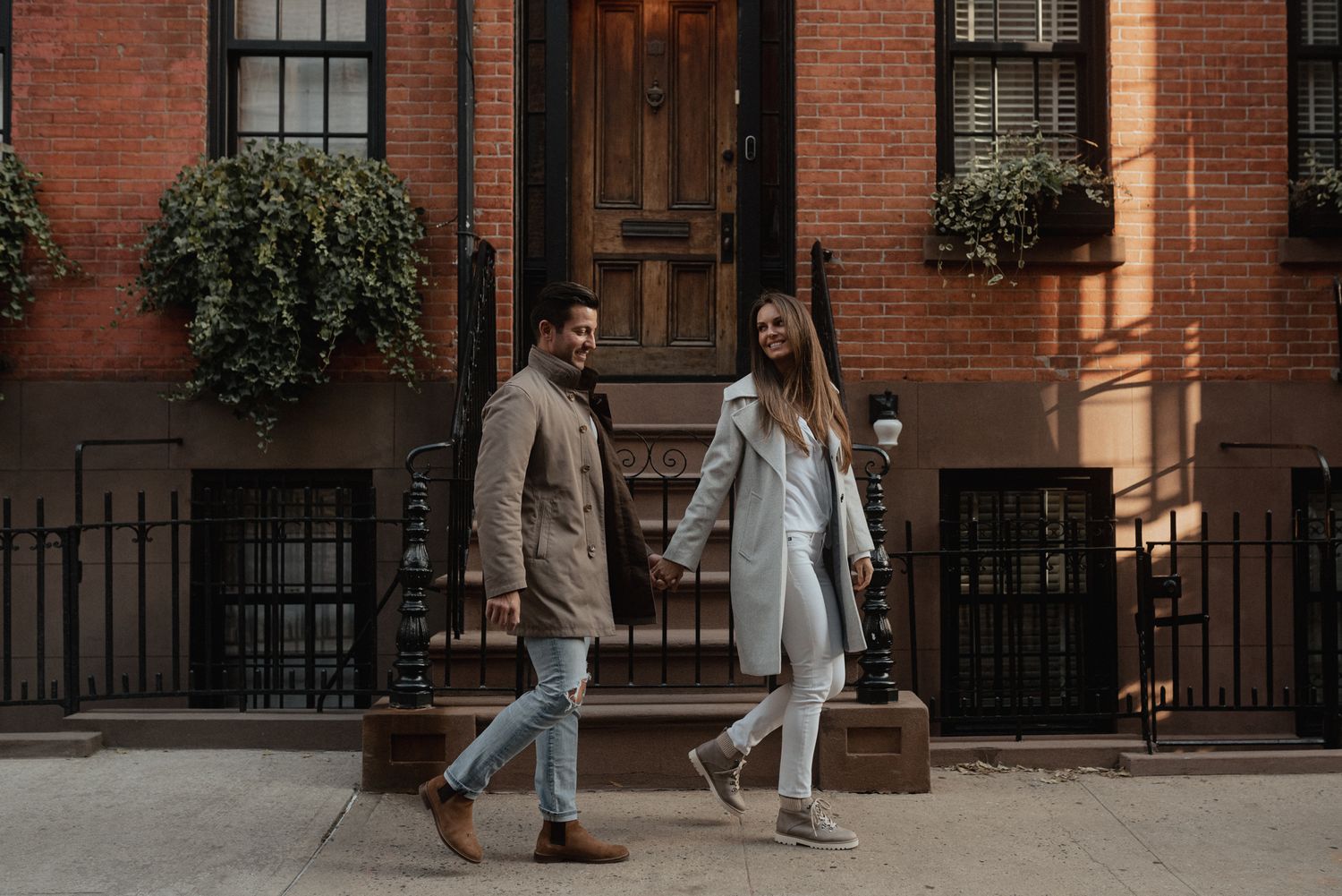 Stylish couple walking past brick townhouses in an urban neighborhood.