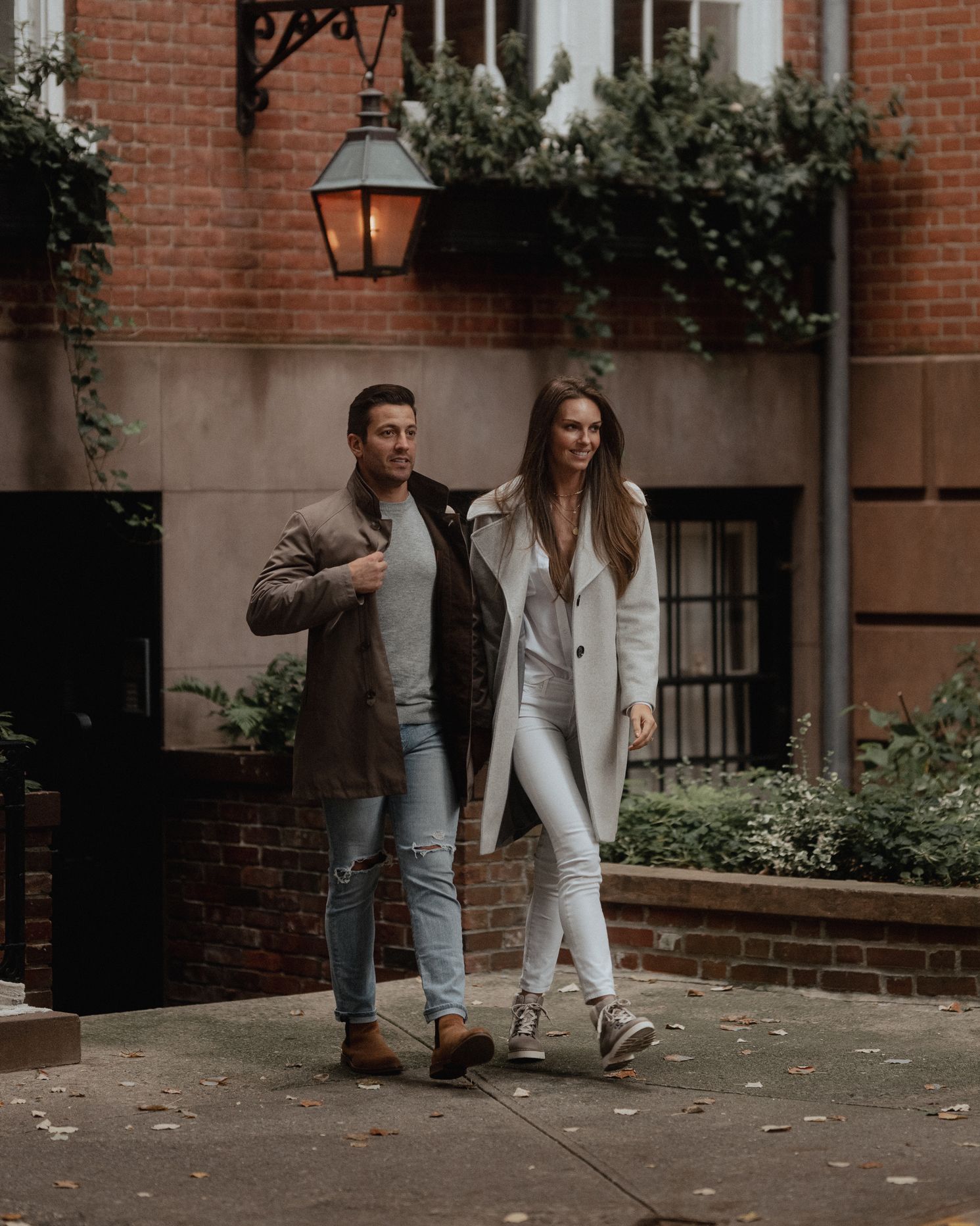 Fashion-forward couple posing against brick building with classic lantern.