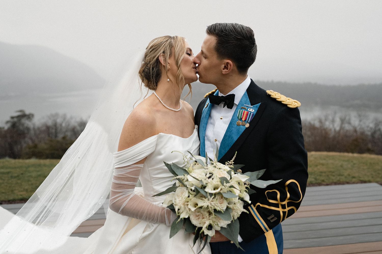 A romantic wedding portrait against a misty mountain backdrop with white floral bouquet.