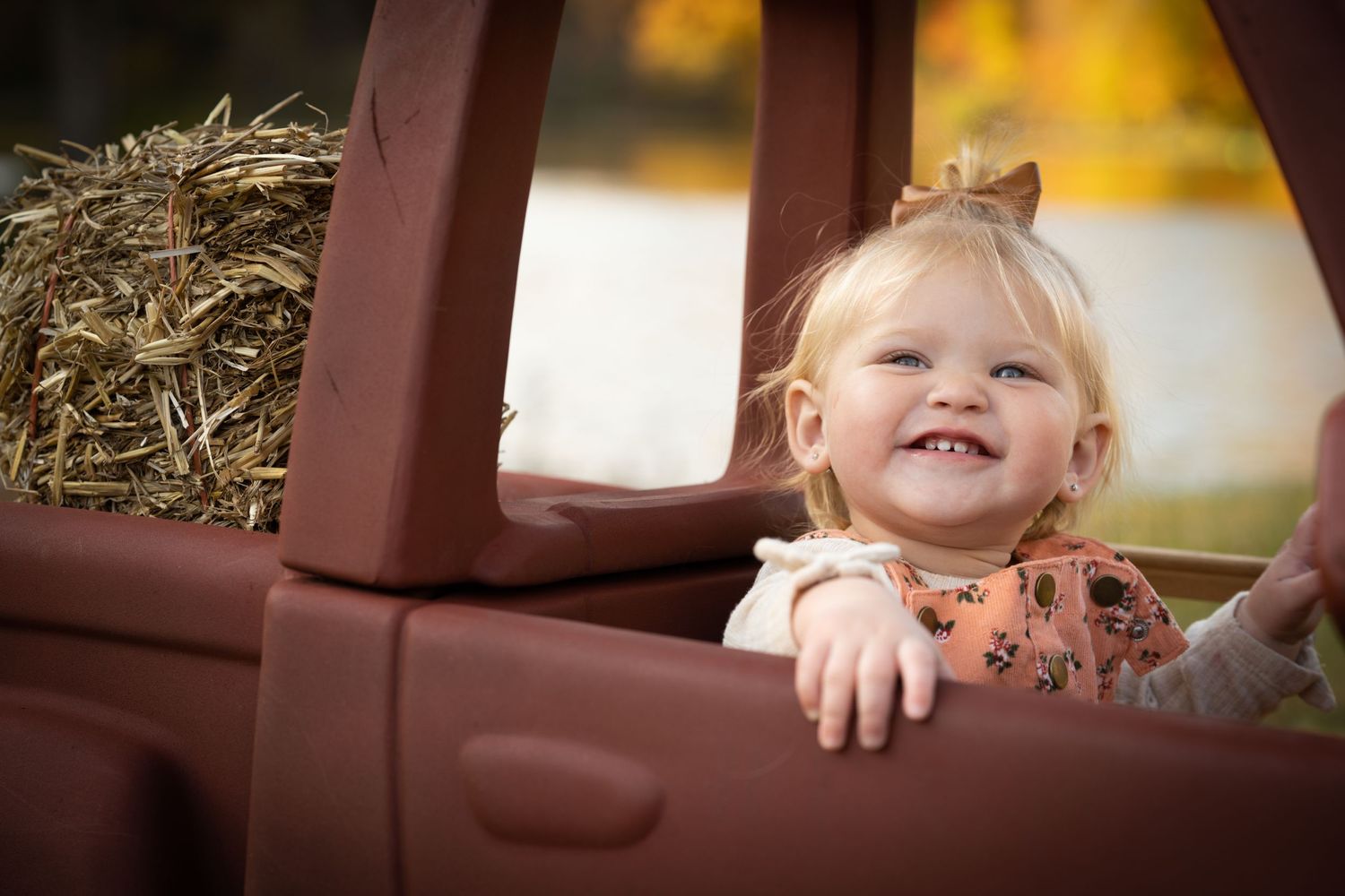 Child peeking out from red vintage toy car during autumn photoshoot.