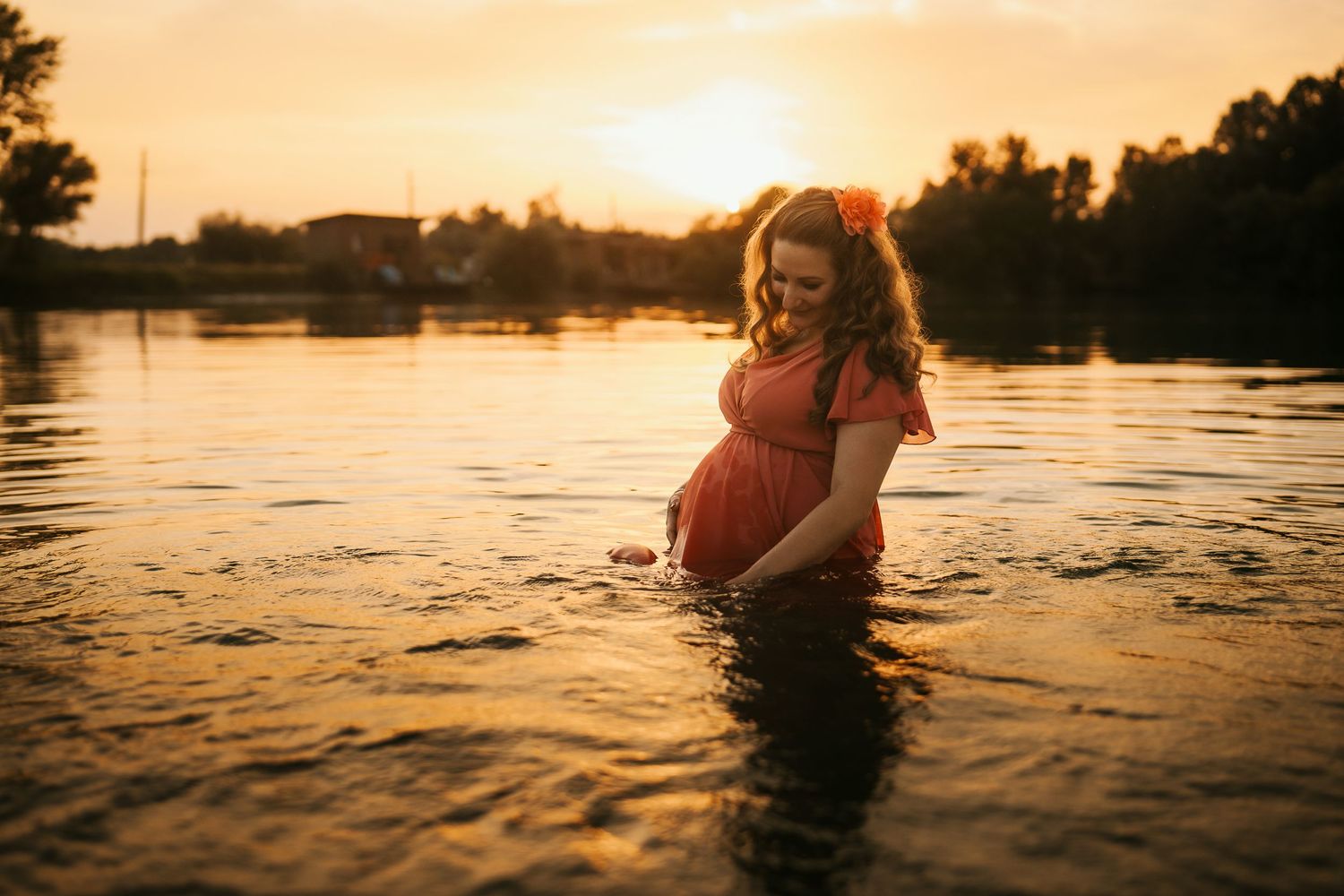 Silhouette of pregnant woman standing in water during golden sunset.