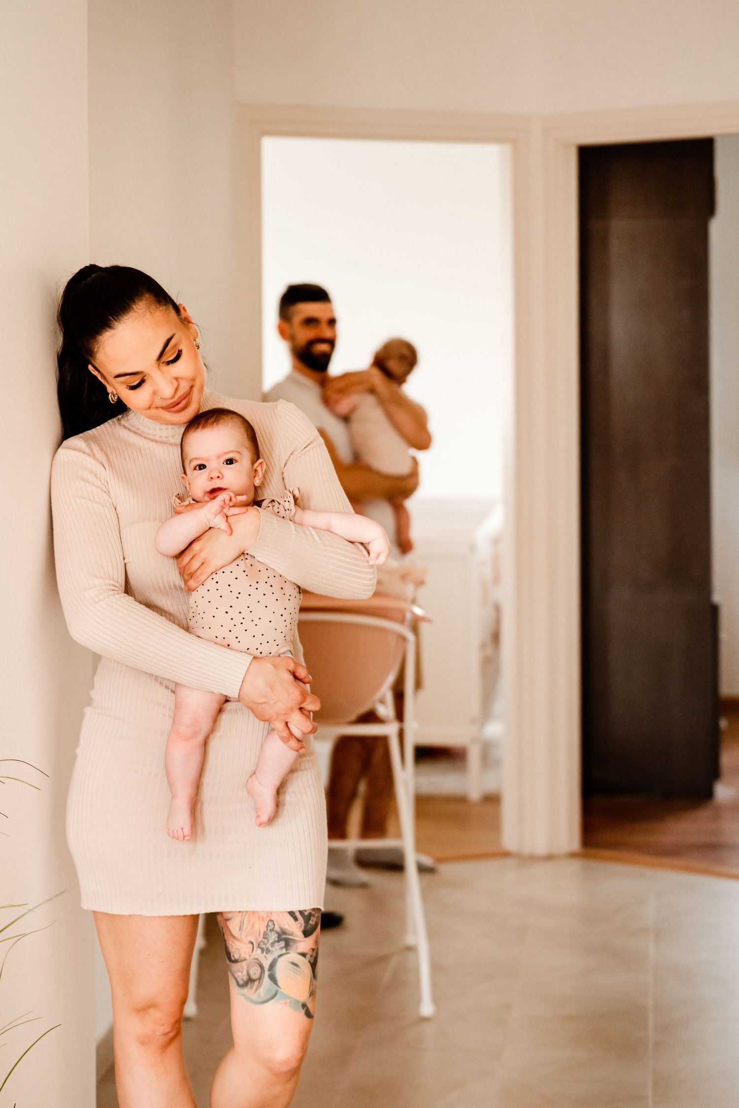 Family portrait in minimalist home interior with mother holding baby in foreground.