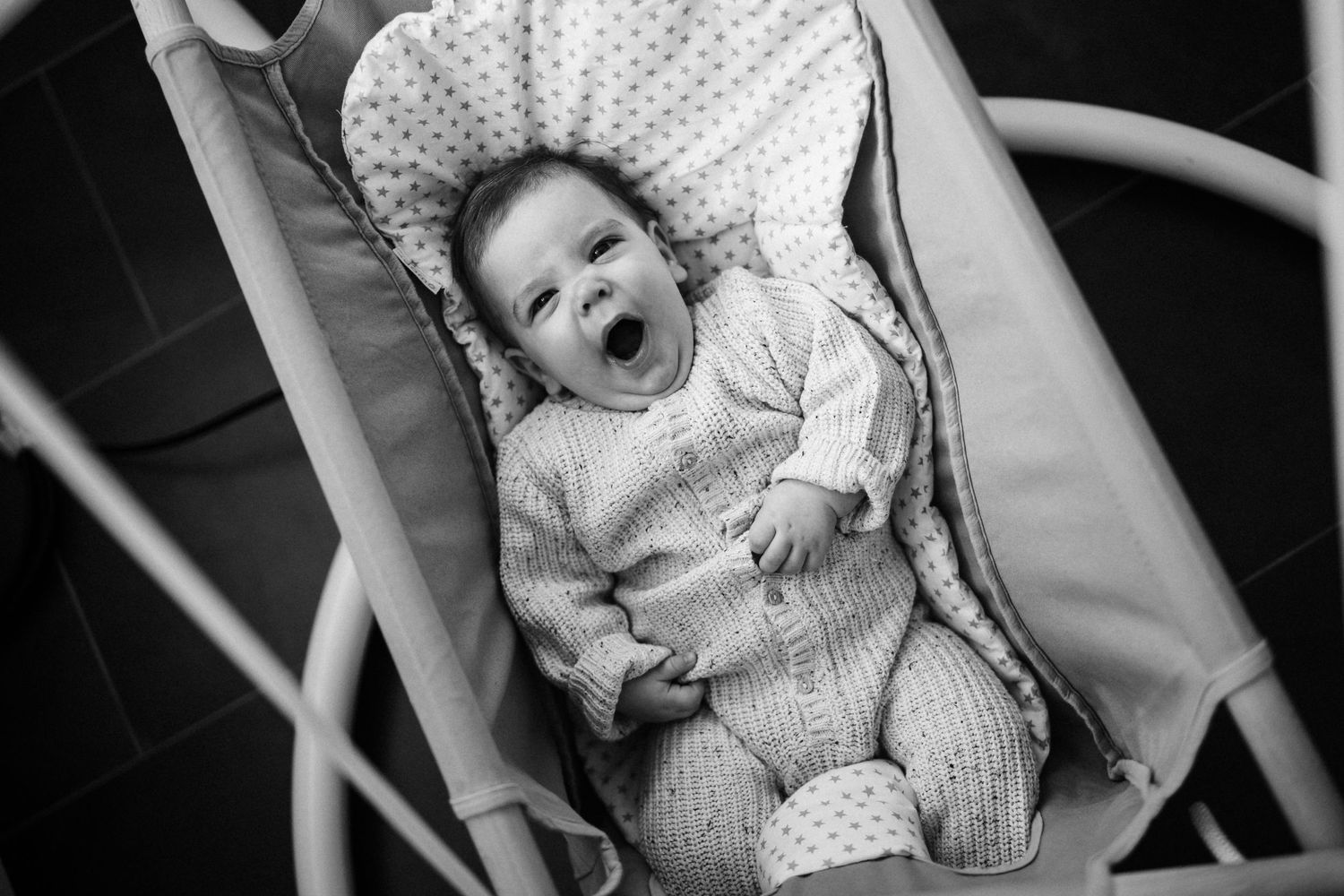 Black and white photo of smiling baby lying in polka dot patterned bouncer seat.