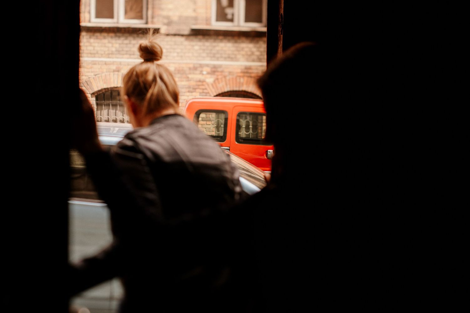 Blurred silhouette watching an orange vehicle through a window frame.