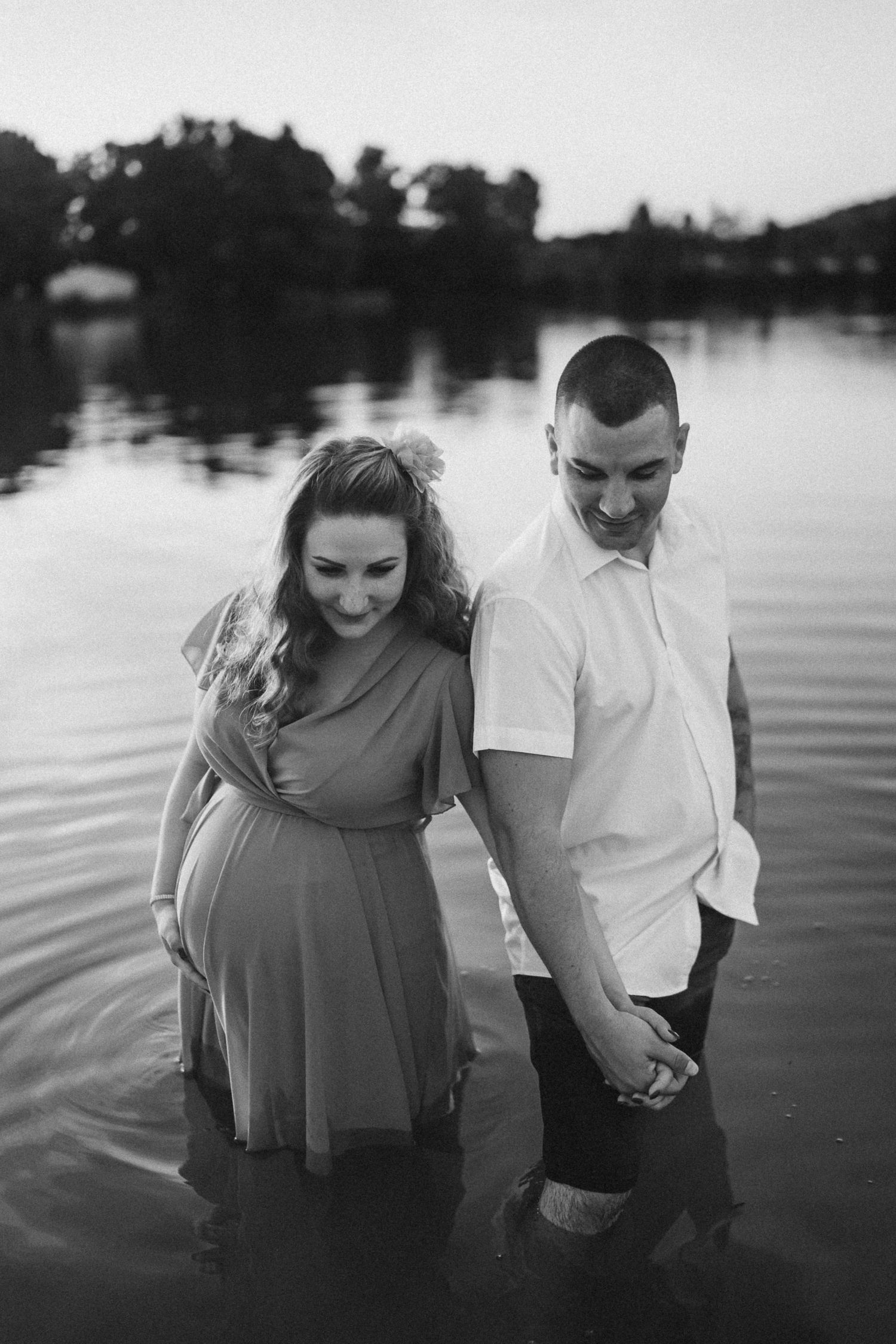 A couple shares an intimate black and white moment while standing in water at dusk.