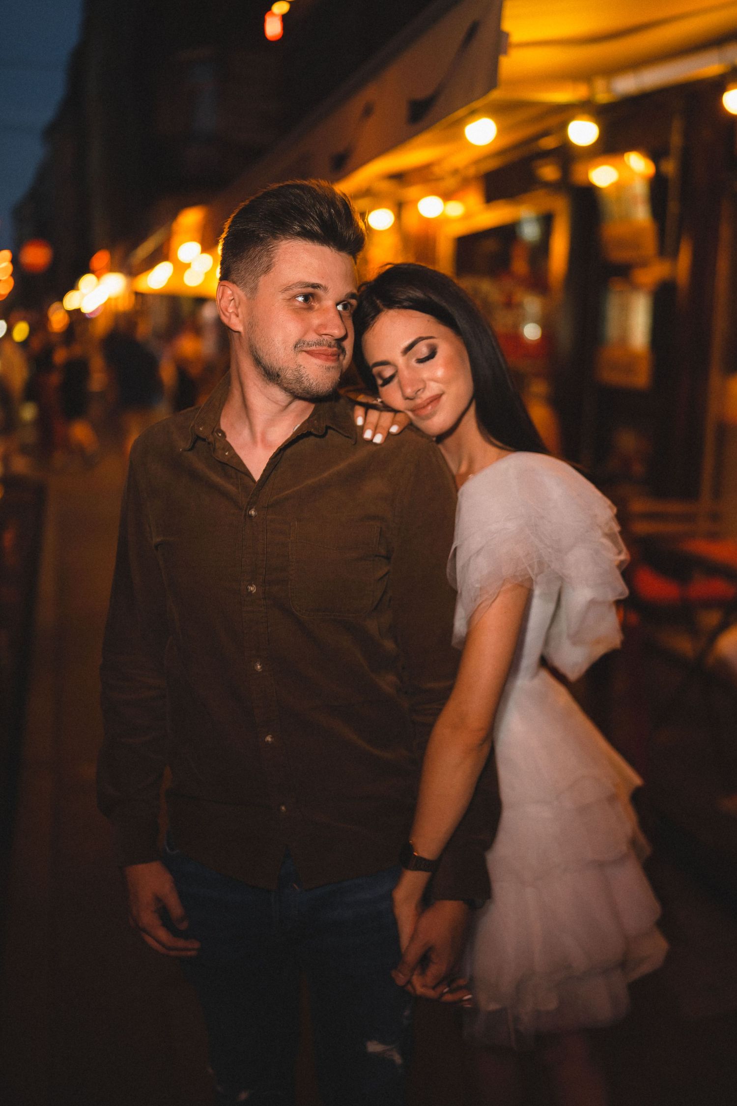 A romantic couple embracing under warm evening lights outside a restaurant.