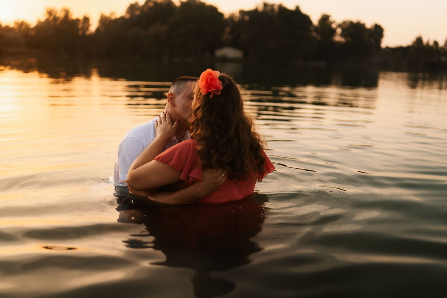 A person in a red dress floats gracefully in calm water during golden hour sunset.
