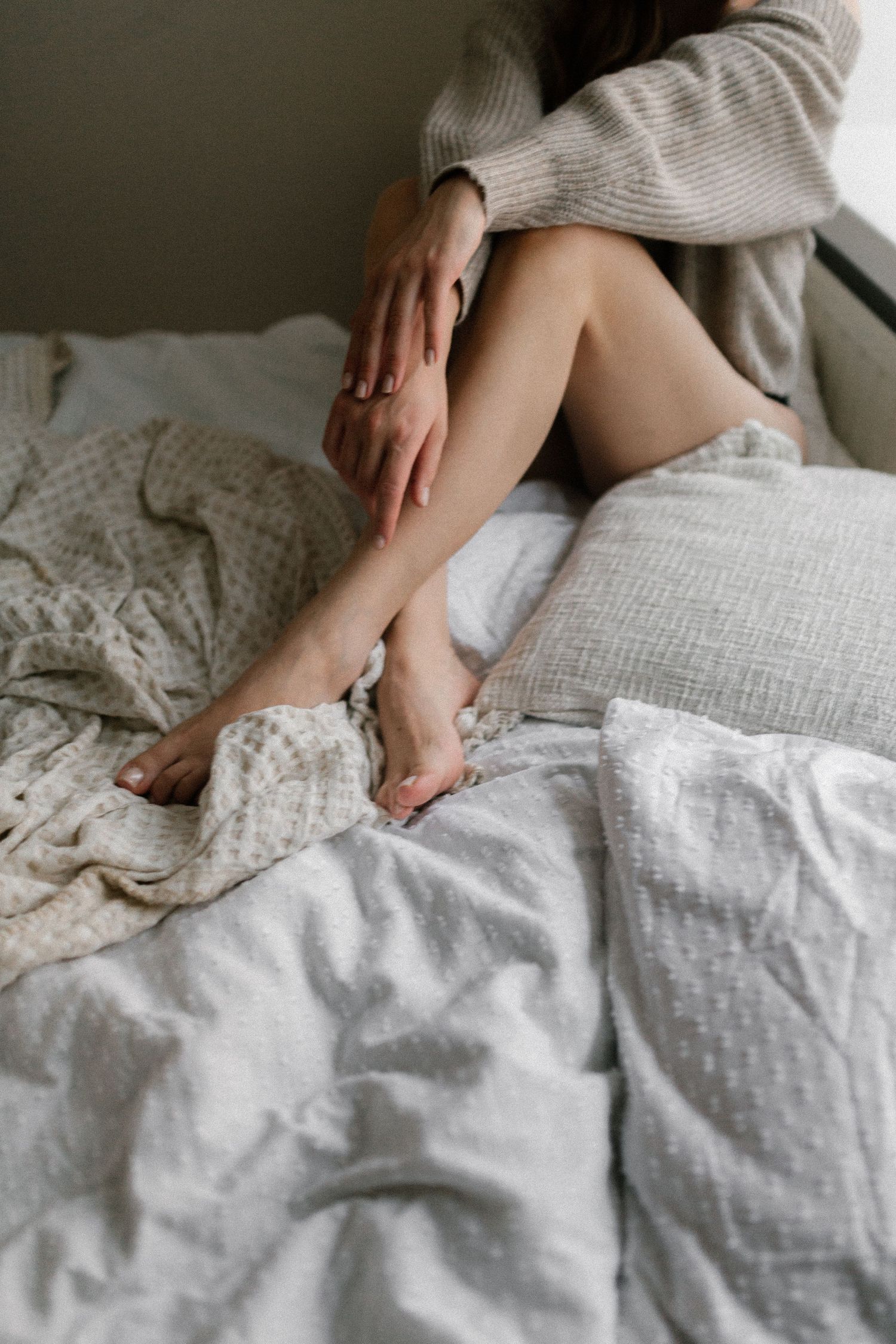 Boudoirvalokuva jossa näkyy sängyllä risti-istunnassa istuvan naisen sääret ja kädet