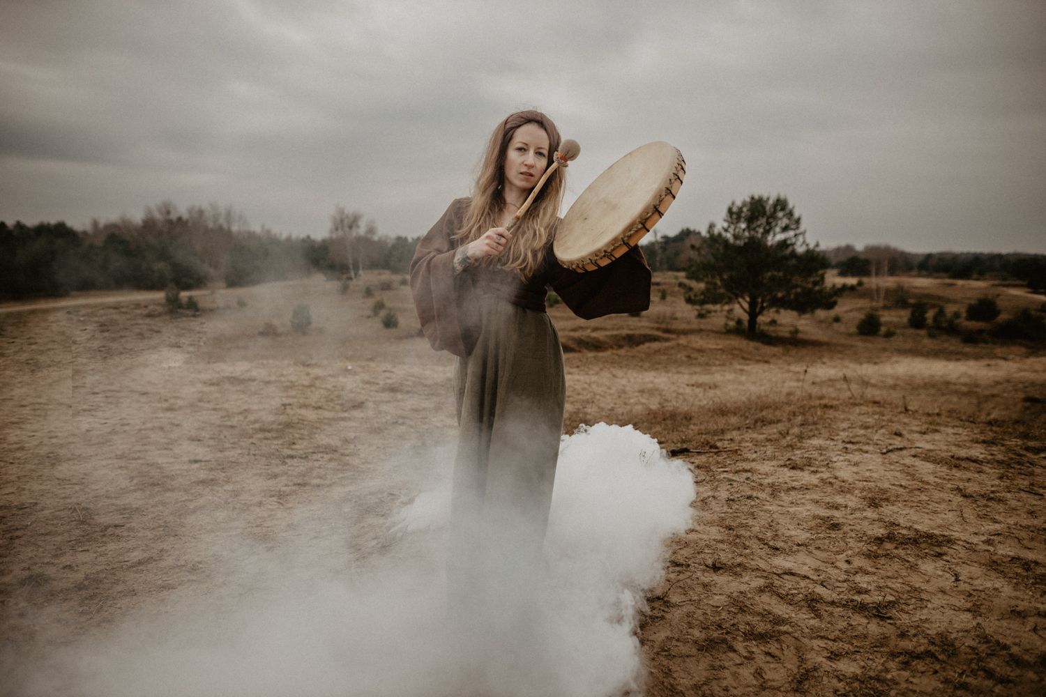 Atmospheric scene of mystic holding ceremonial drum in foggy landscape.