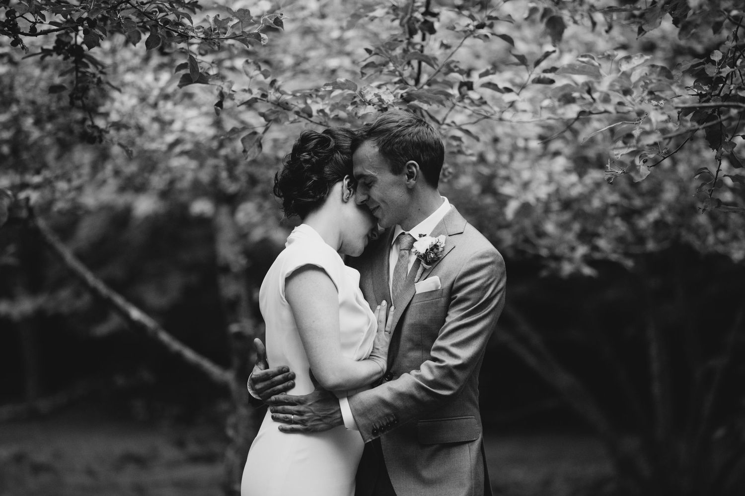 A romantic black and white wedding photo showing a bride and groom sharing a quiet moment in a outdoor garden setting.