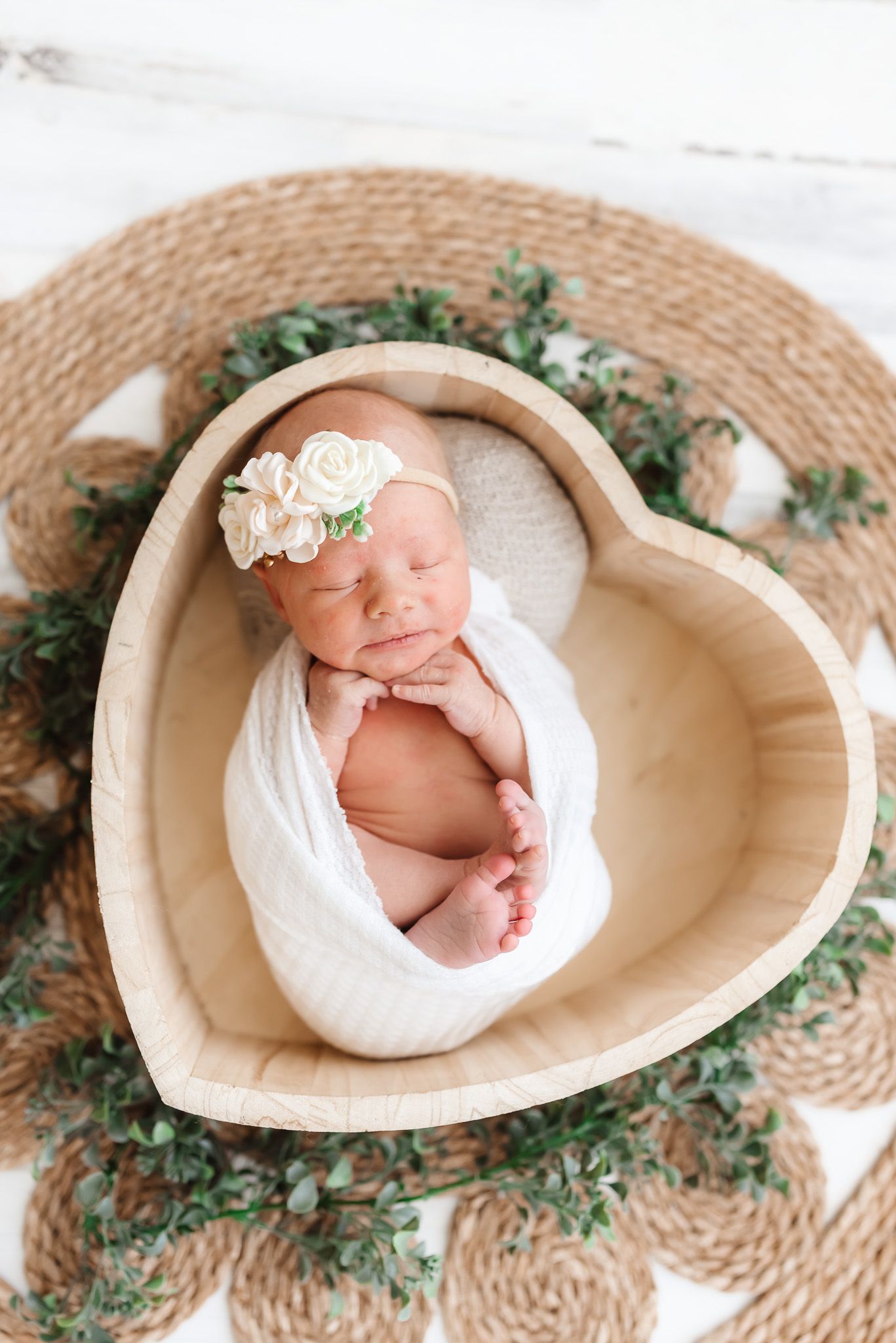 Newborn photography series showing a sleeping baby wrapped in white fabric nestled in a woven basket with greenery.
