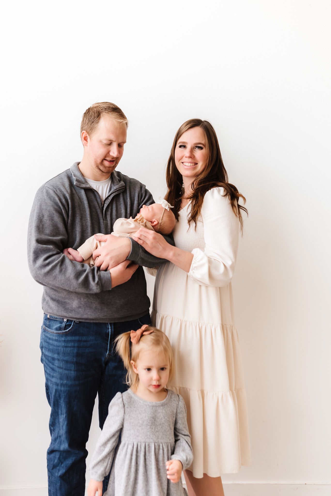 Family poses together against white backdrop in coordinating neutral colored outfits.
