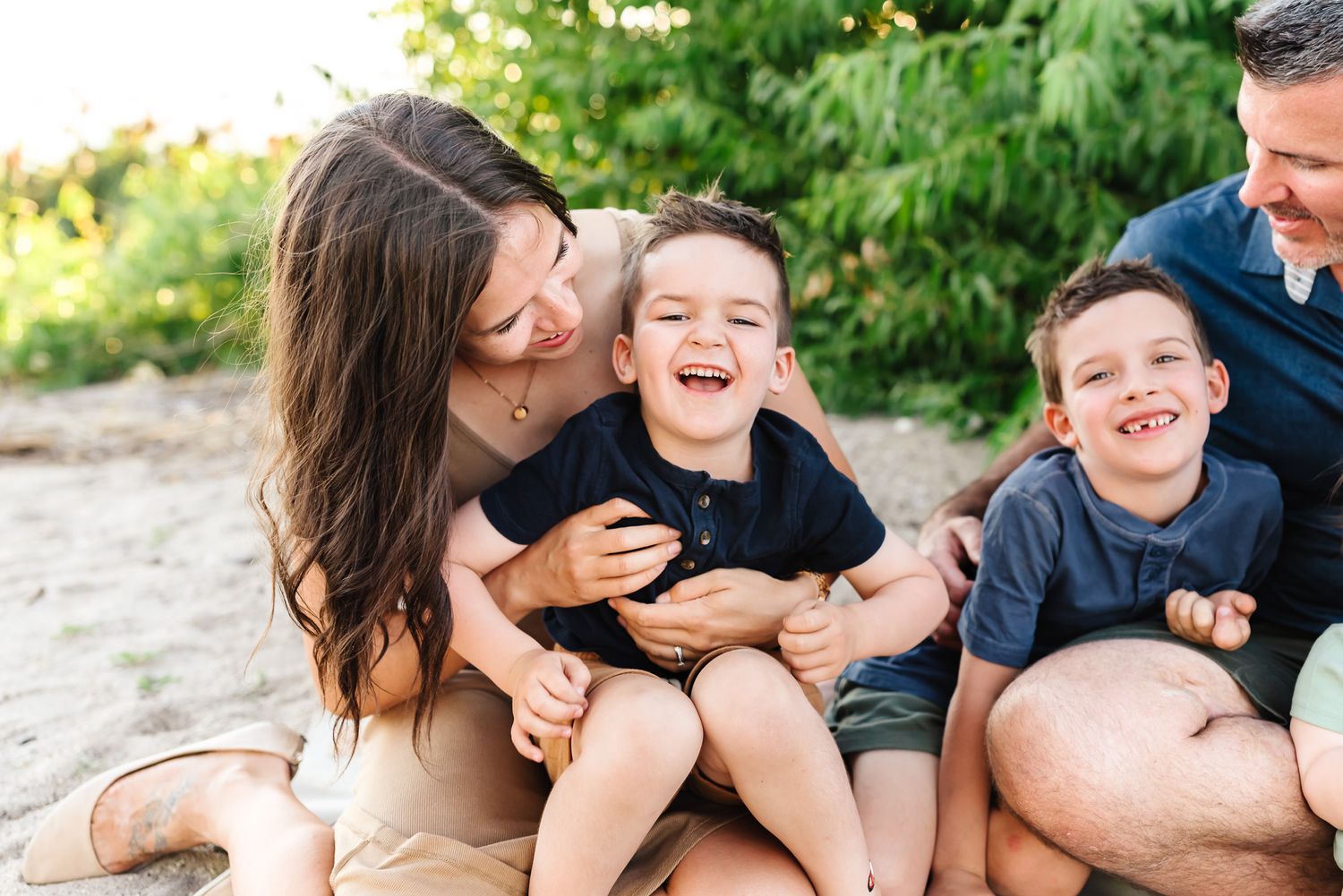 Family playing and laughing together on a beach during a casual photo session.