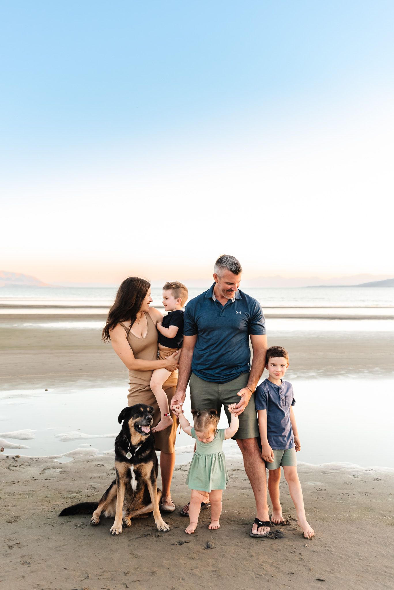 Family and their dog posing together on a scenic beach at sunset.