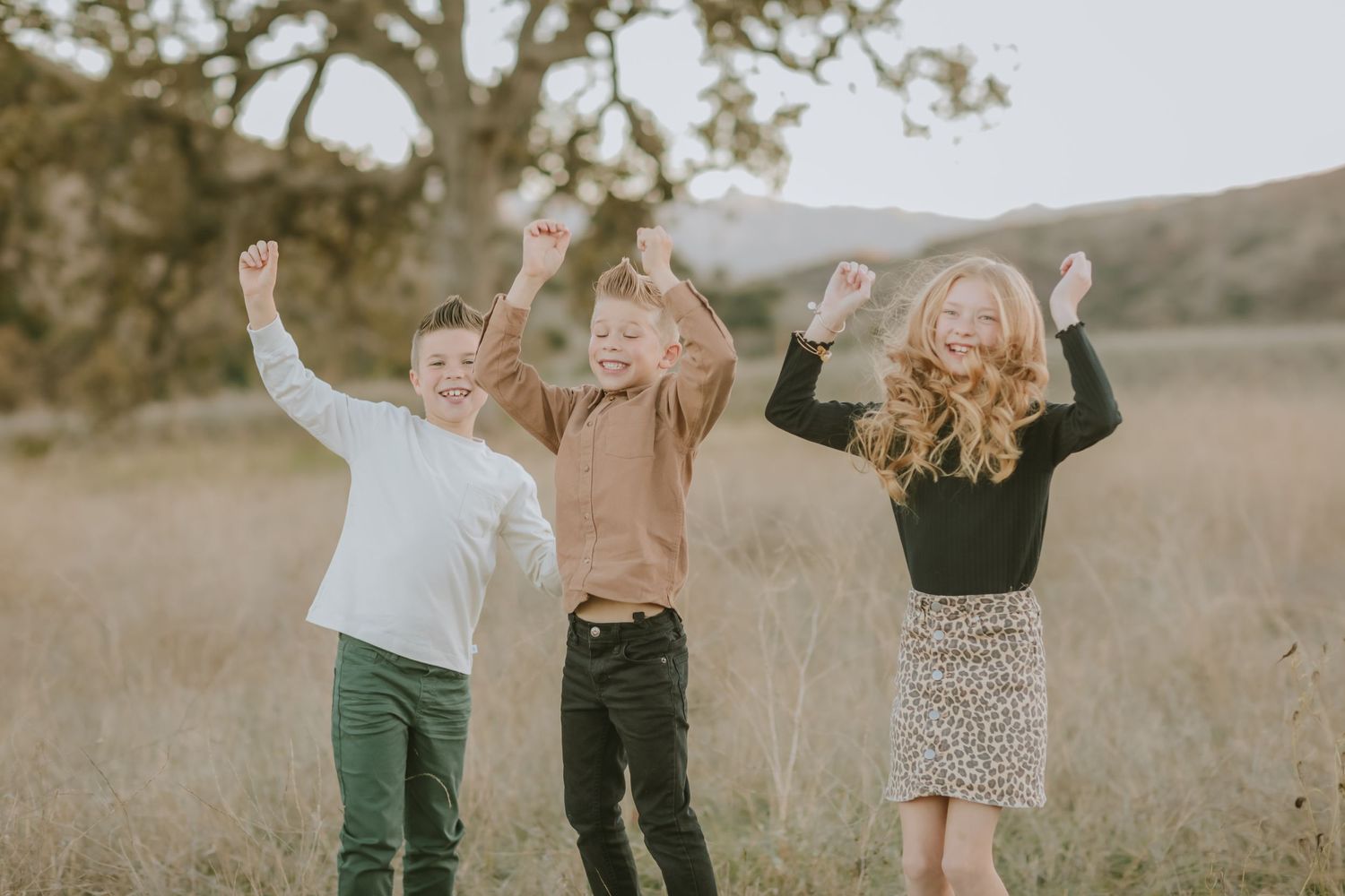 Three people jumping with joy in a sunny meadow with trees in the background.