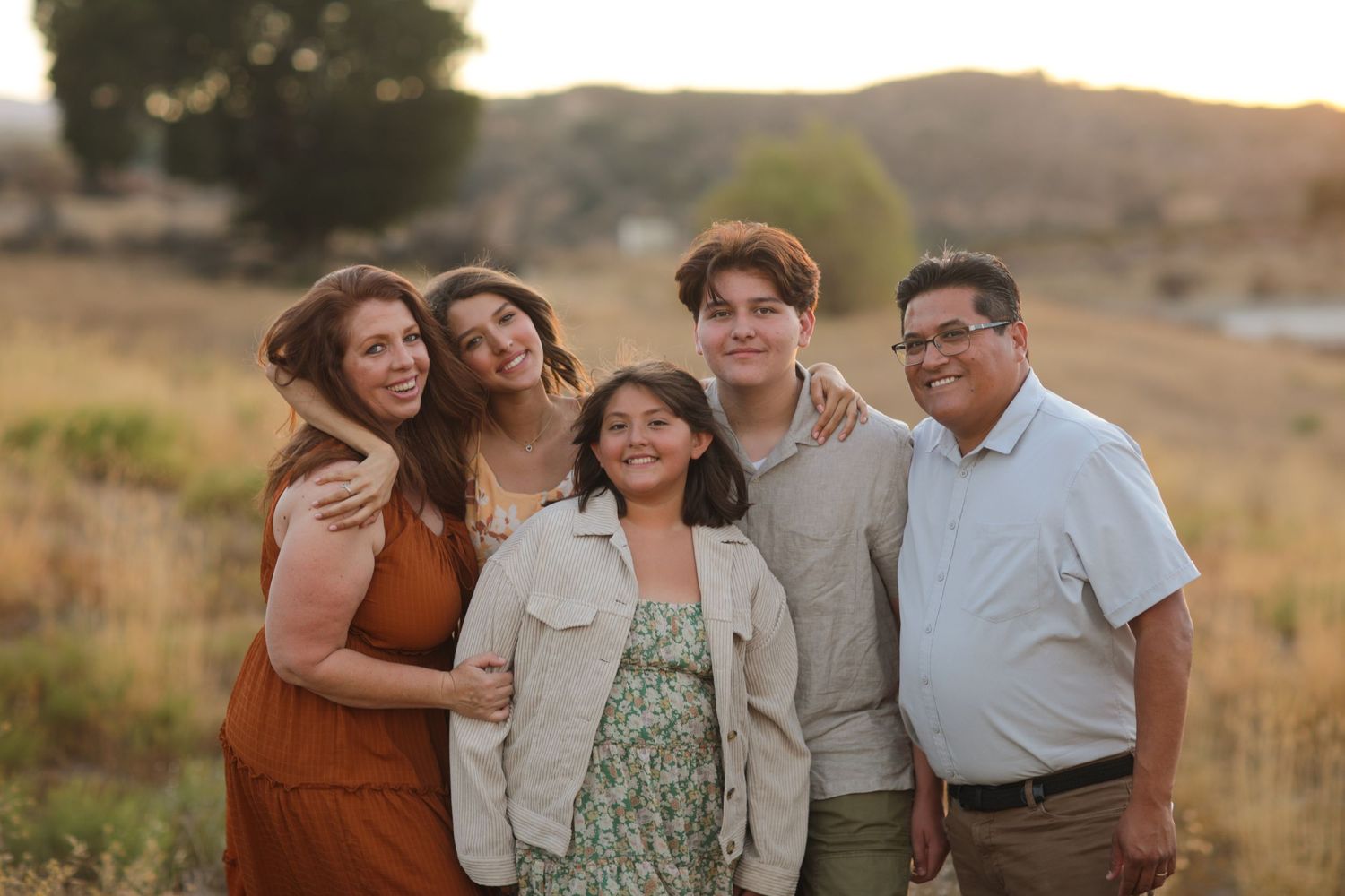 A cheerful family portrait taken at golden hour in a rustic outdoor setting.