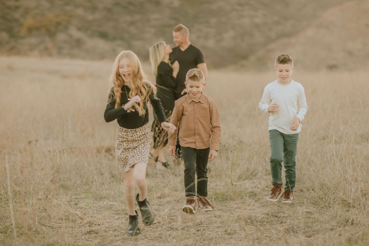 Children running playfully through a golden grass field at sunset.